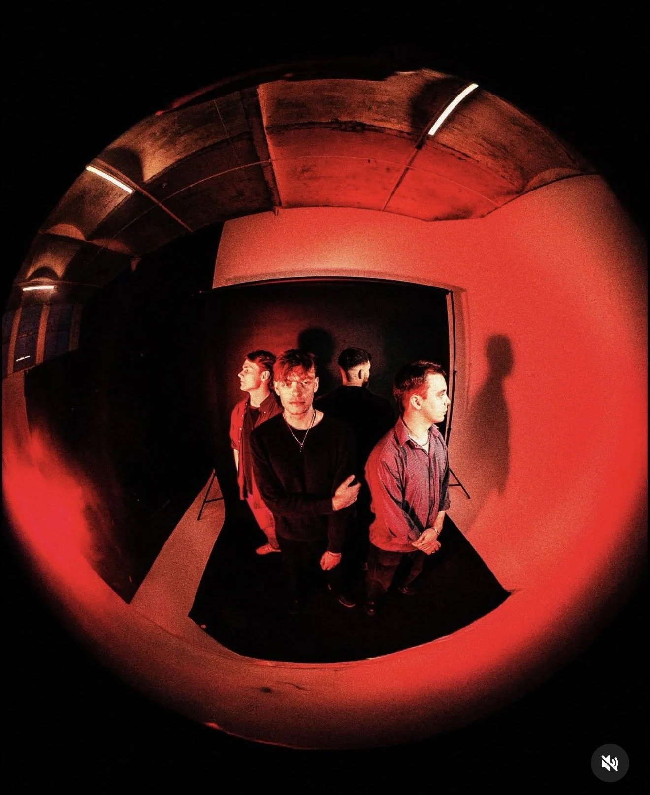 A fisheye shot of four men standing in a dark studio with red lighting, empty ceiling, and black backdrop.