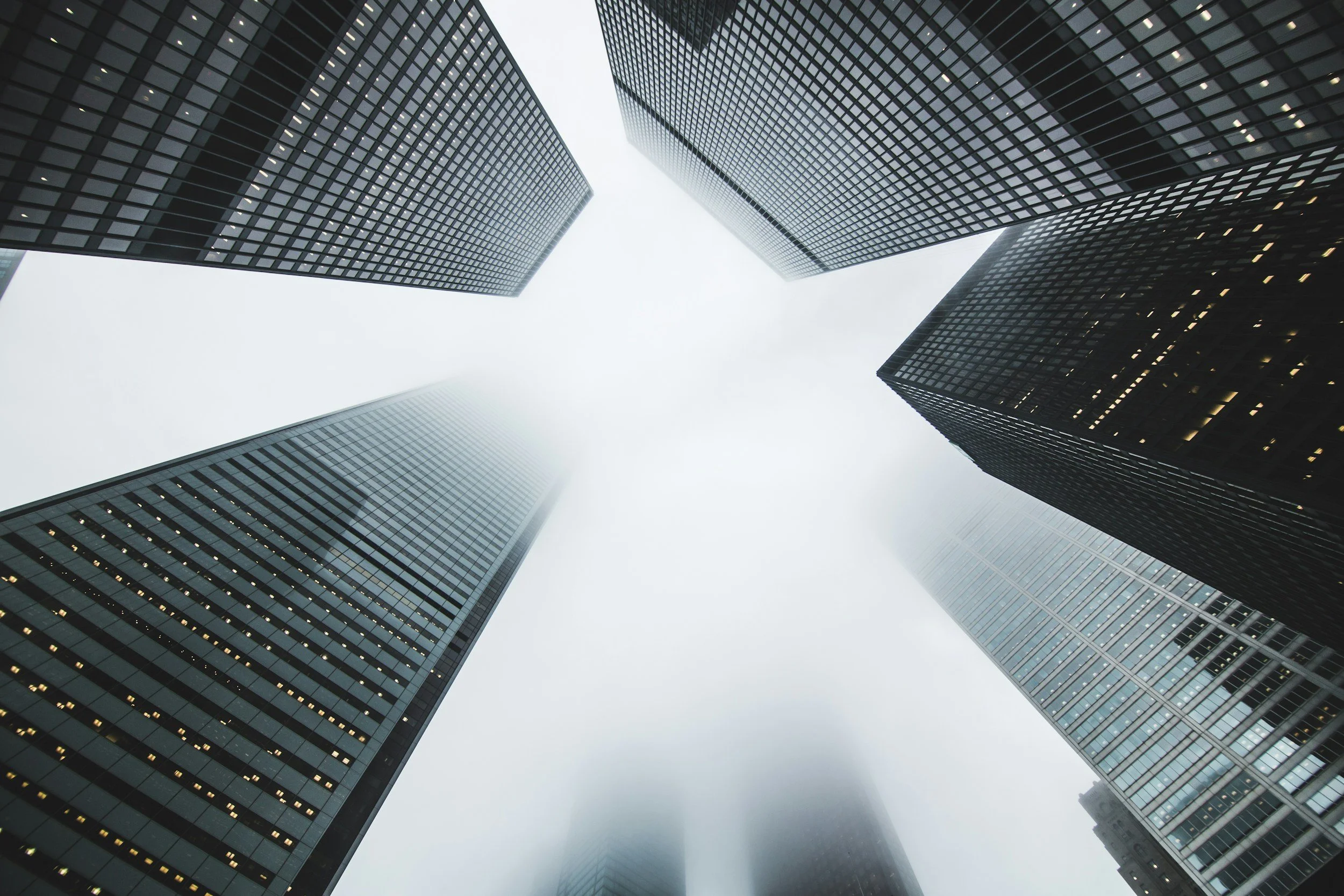 Looking up at tall skyscrapers with glass facades in a city on a foggy day