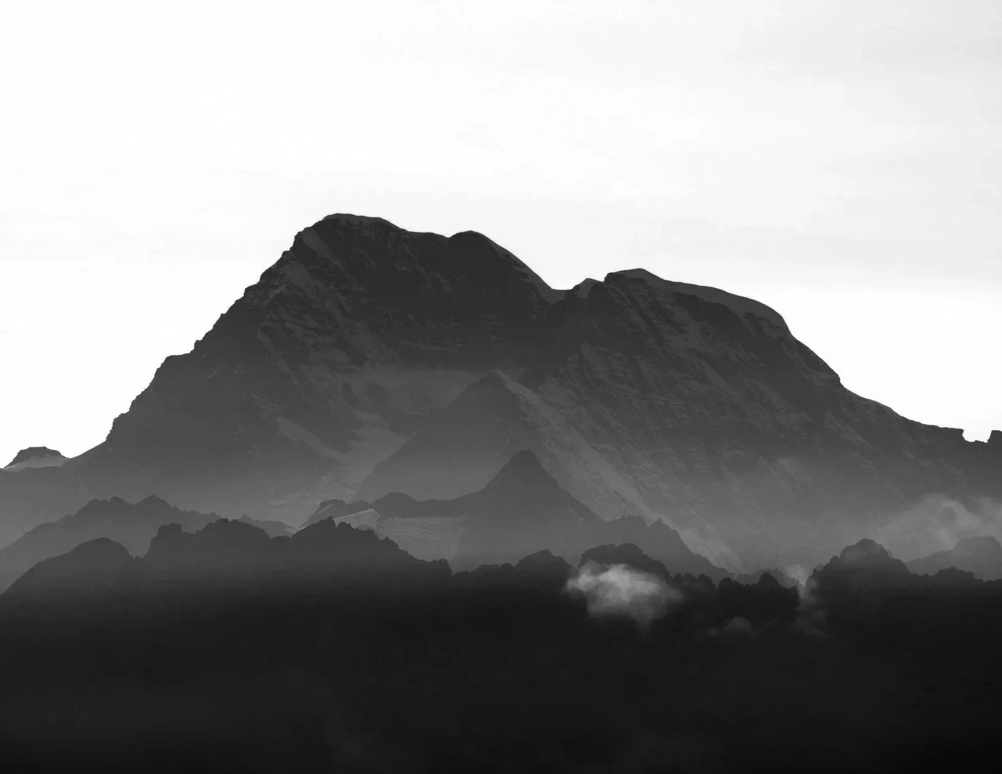 Black and white photograph of a large mountain with layered ridges and clouds at its base.