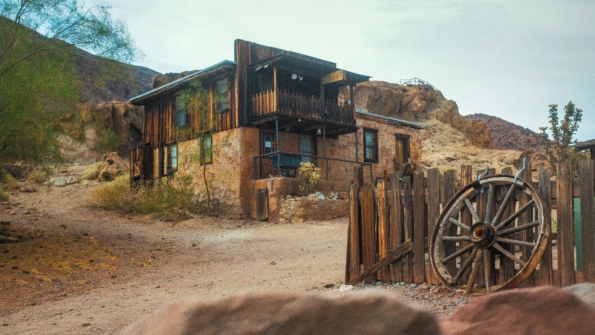 Maison en pierre et bois dans un paysage désertique avec un vieux chariot en bois près de la clôture.