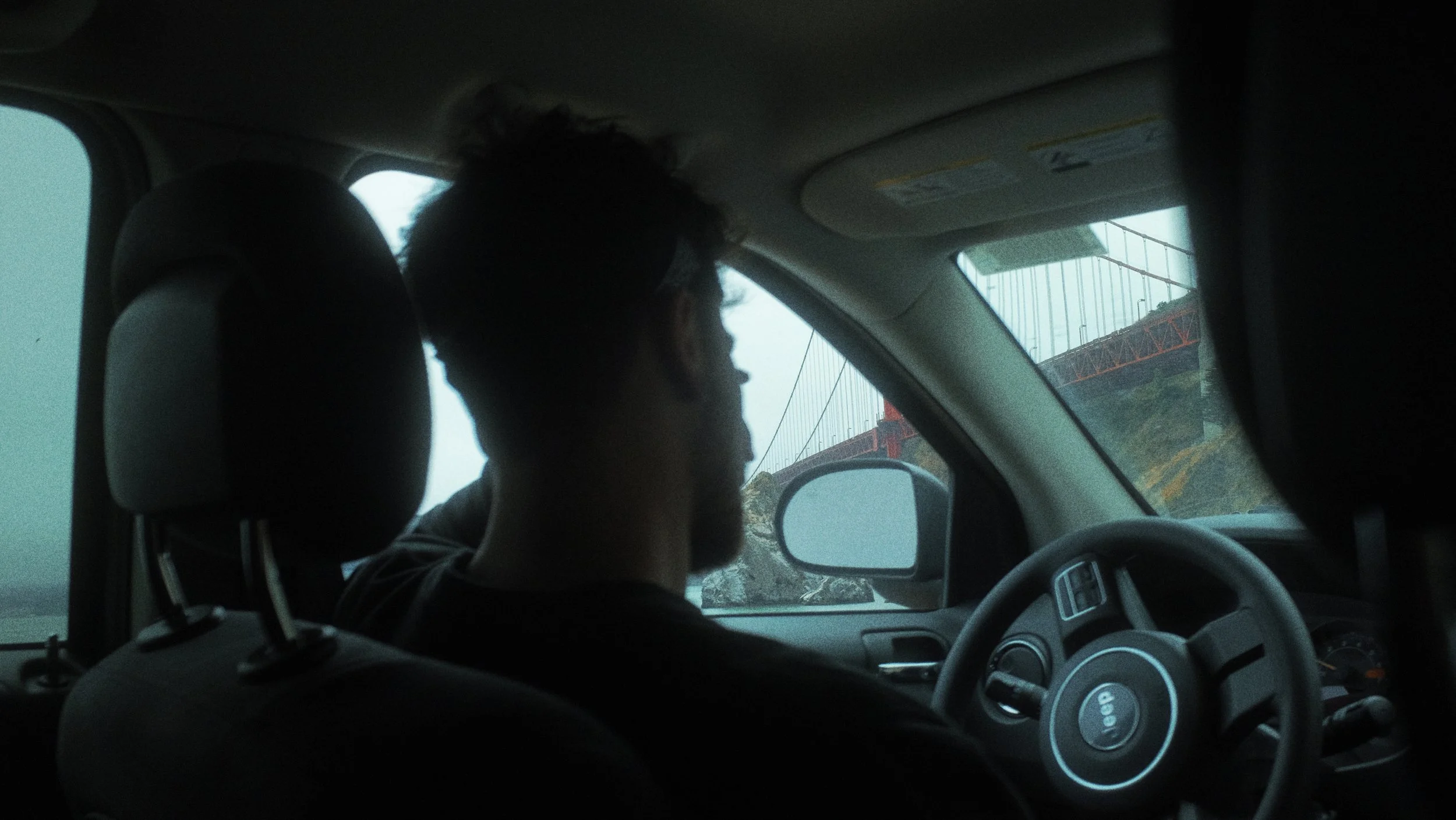 Un homme conduit une voiture avec le pont suspendu de San Francisco visible à travers le pare-brise.