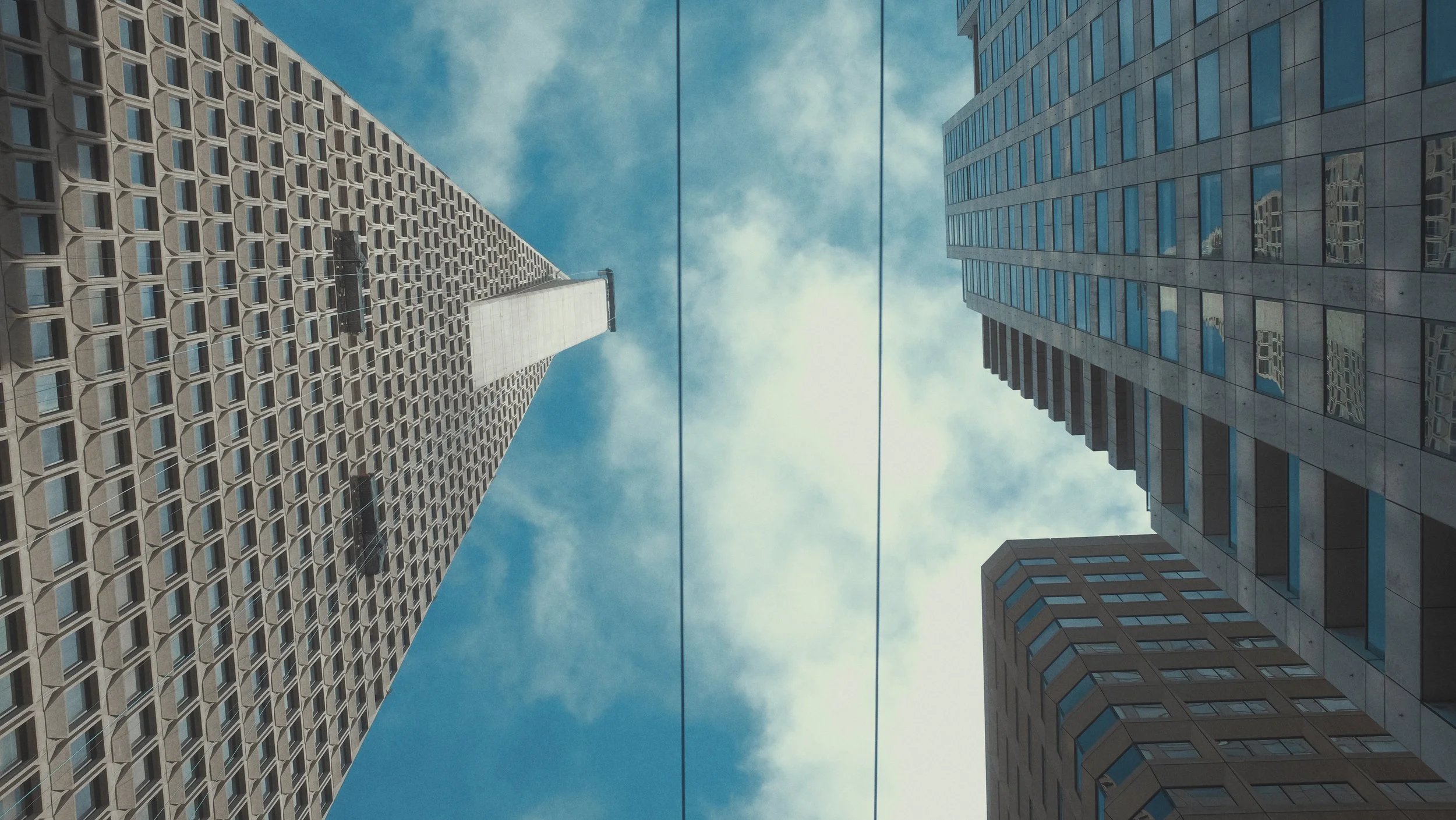 Vue en contre-plongée de trois gratte-ciel modernes sous un ciel partiellement nuageux.