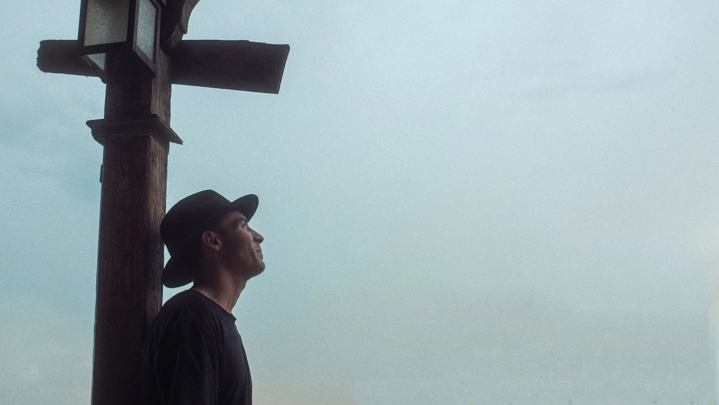 Un homme portant un chapeau noir et un t-shirt noir regarde vers le haut à côté d'un grand panneau en bois.