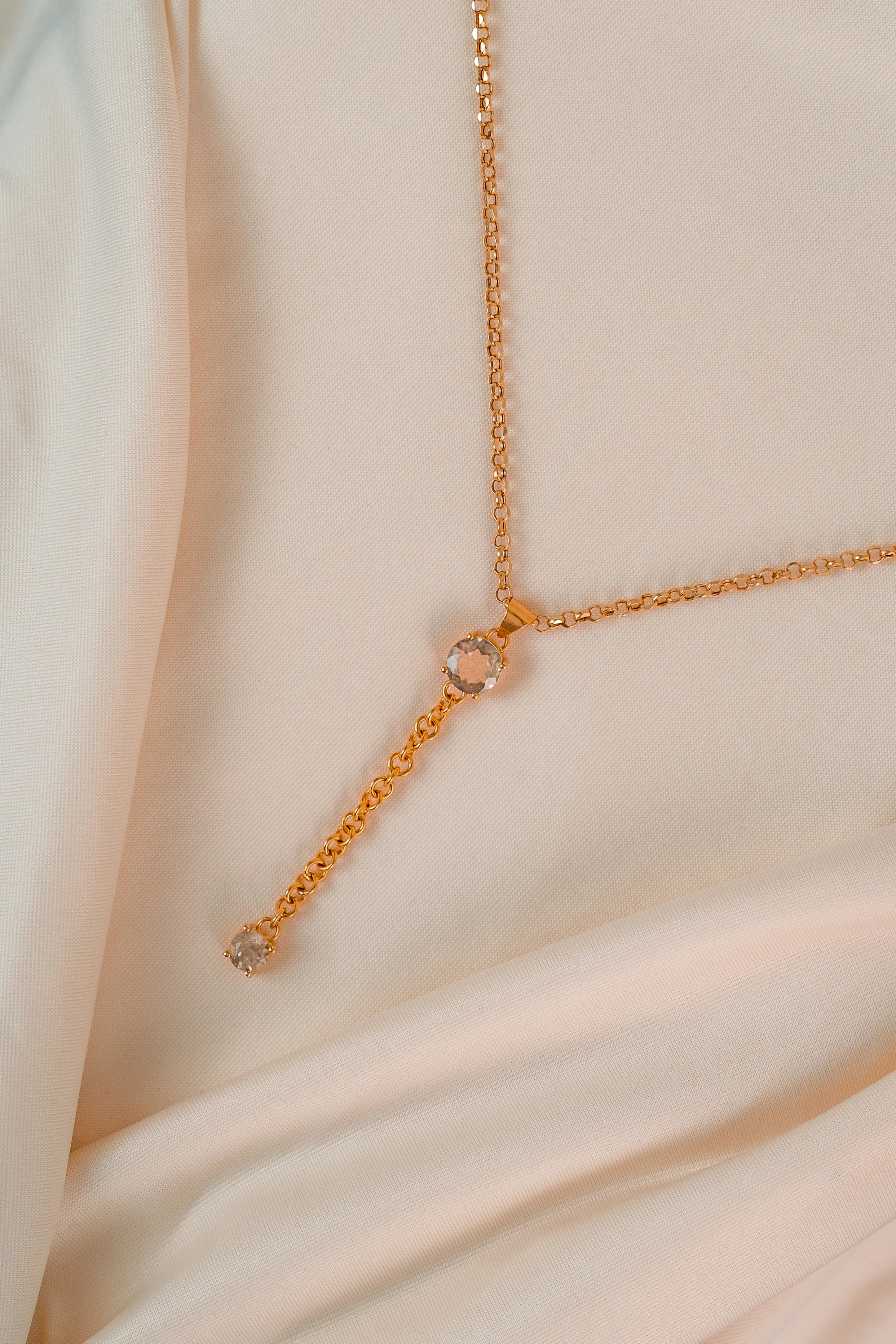 Gold chain necklace with three gemstones on a light fabric background.