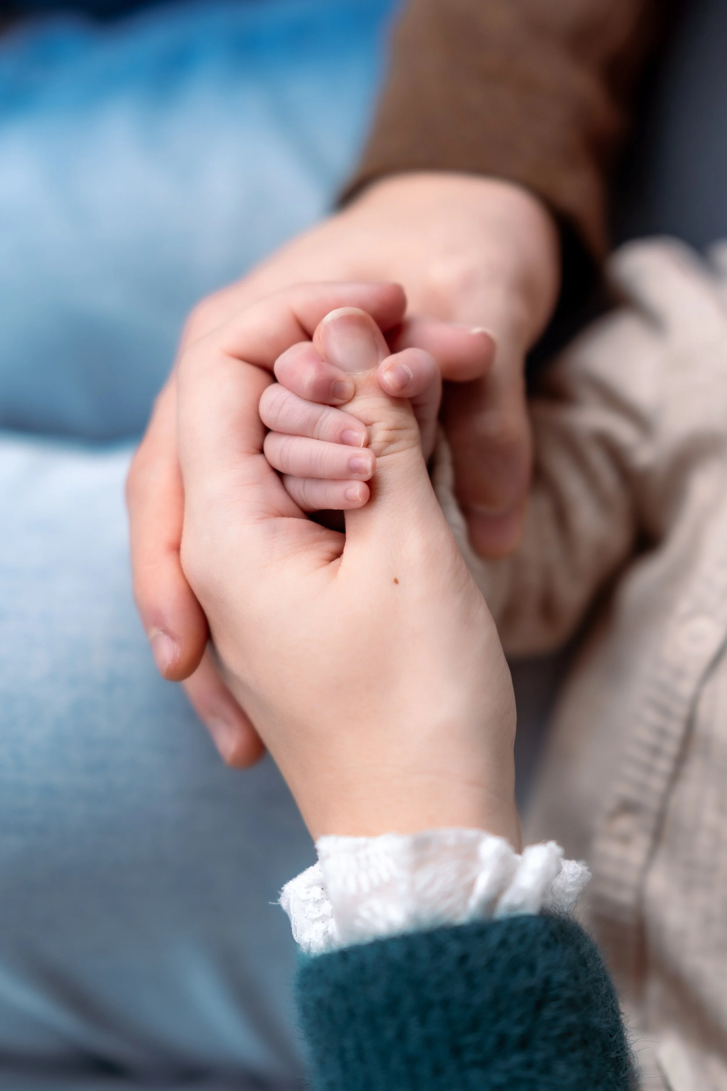 A close-up of a baby holding an adult's finger, with the adult's hand gently grasping the baby's smaller hand.