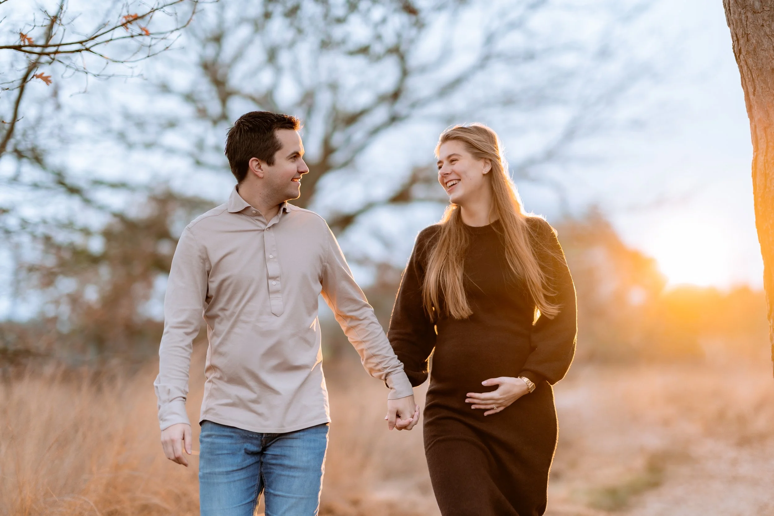 A couple walking outdoors holding hands during sunset, smiling at each other.