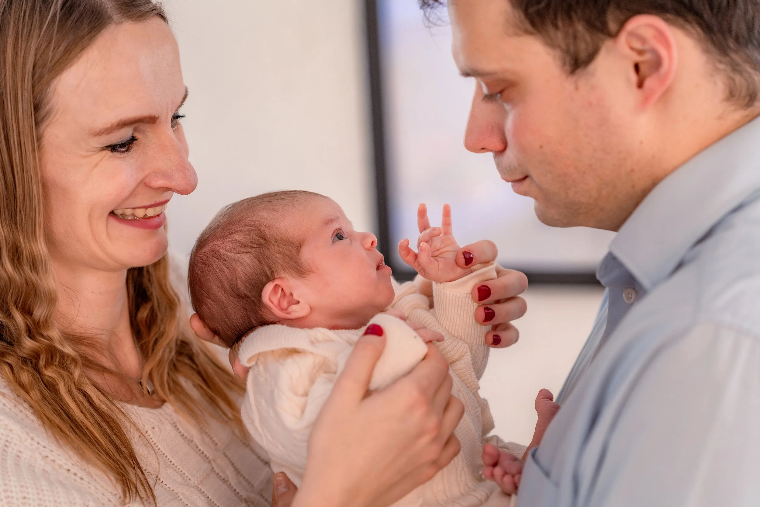 A mother and father holding their baby, looking at each other and the baby with affection in a close-up shot.