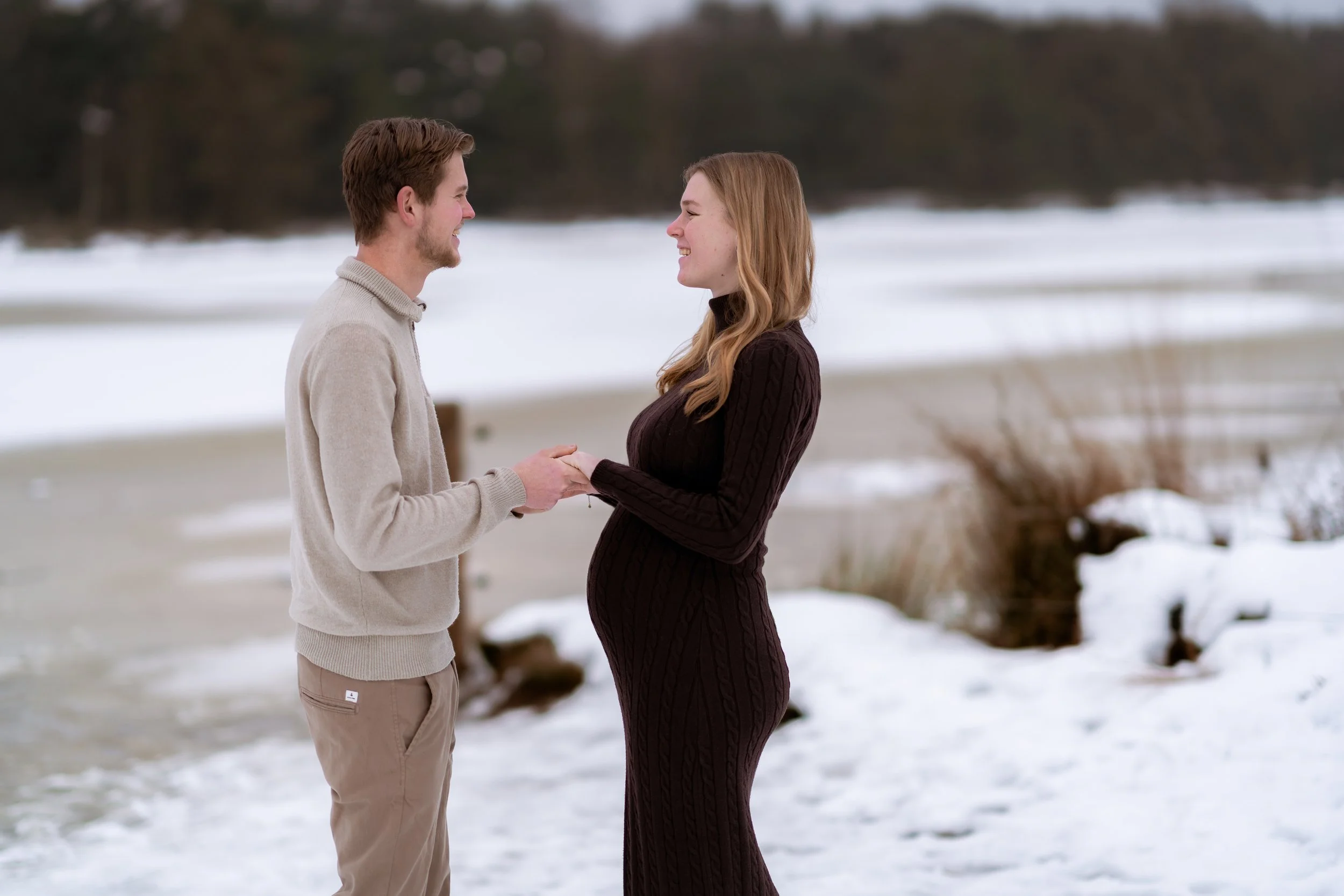 A couple holding hands on a snowy beach, facing each other and smiling.