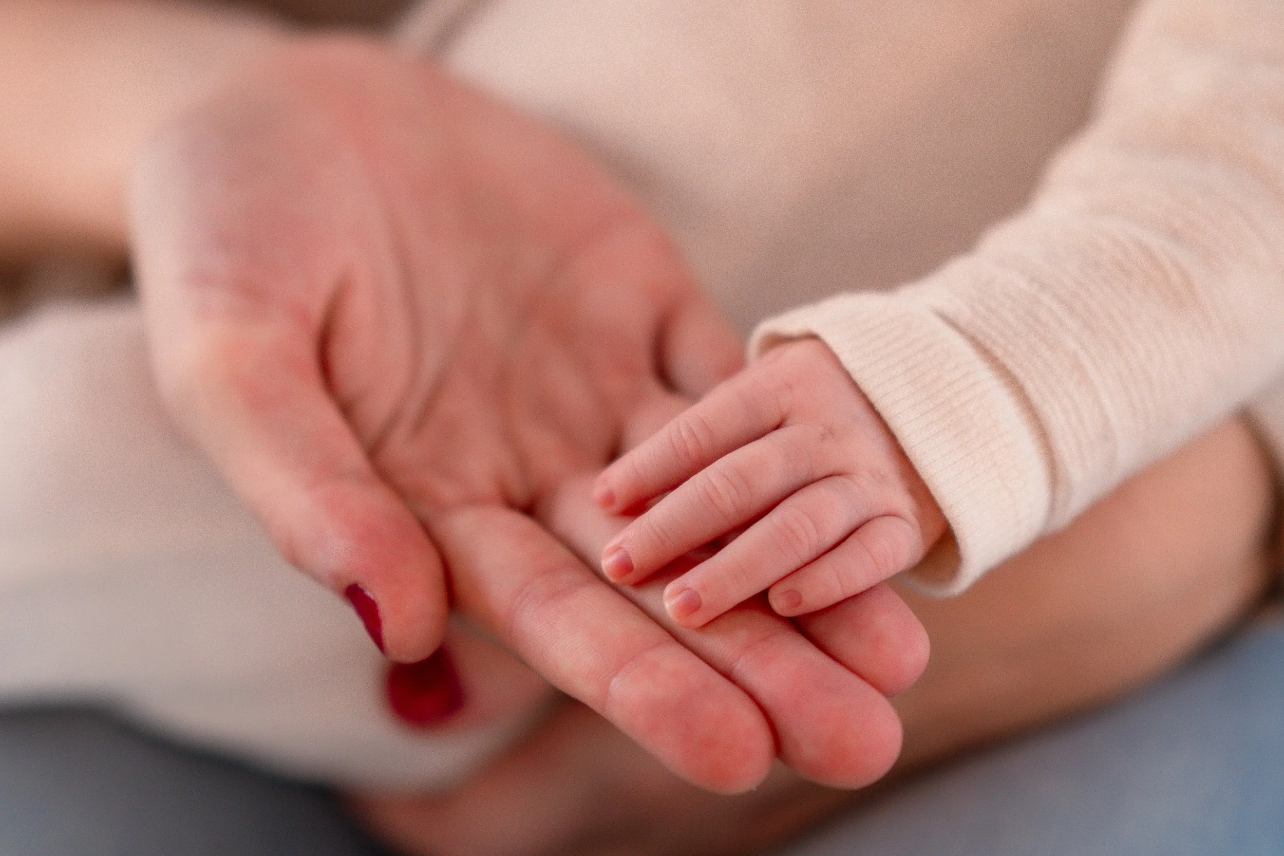 A close-up of an adult's hand holding a child's hand, showing the adult's hand with painted nails and the child's smaller hand resting gently on the adult's palm.