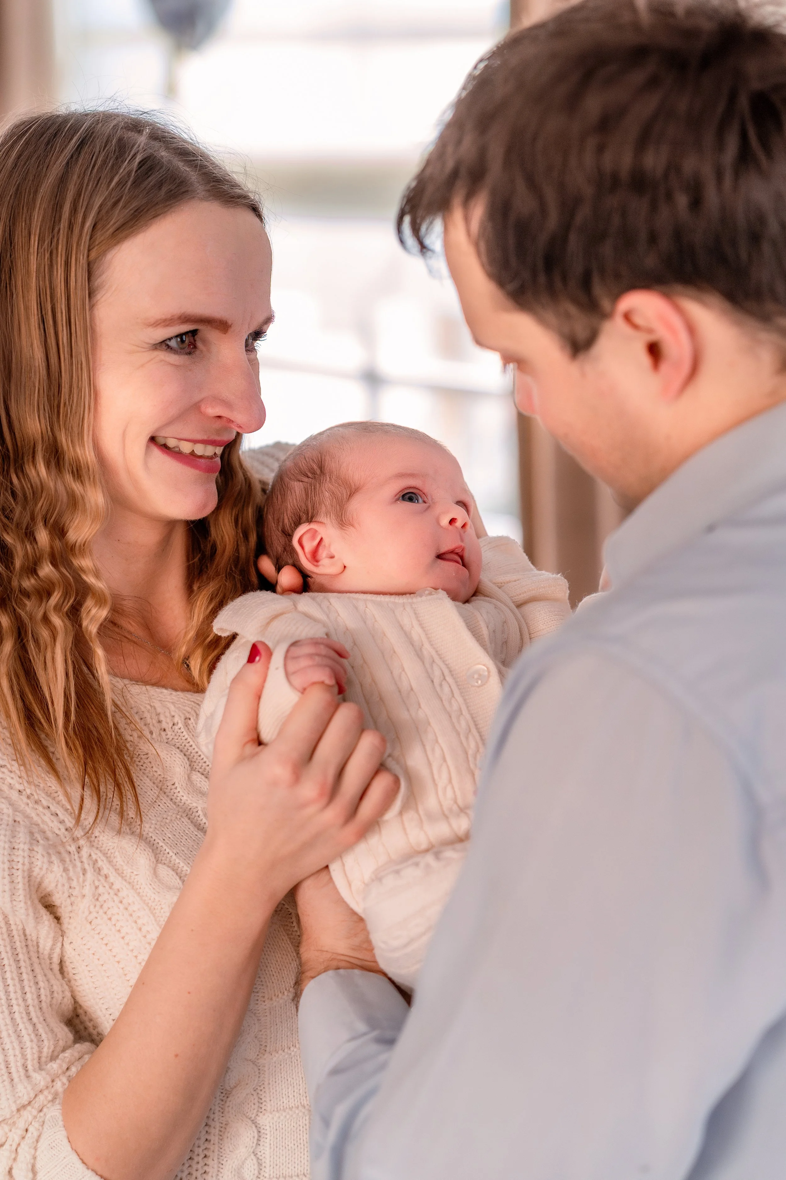 A happy woman and a man hold a newborn baby, looking into each other's eyes and smiling.