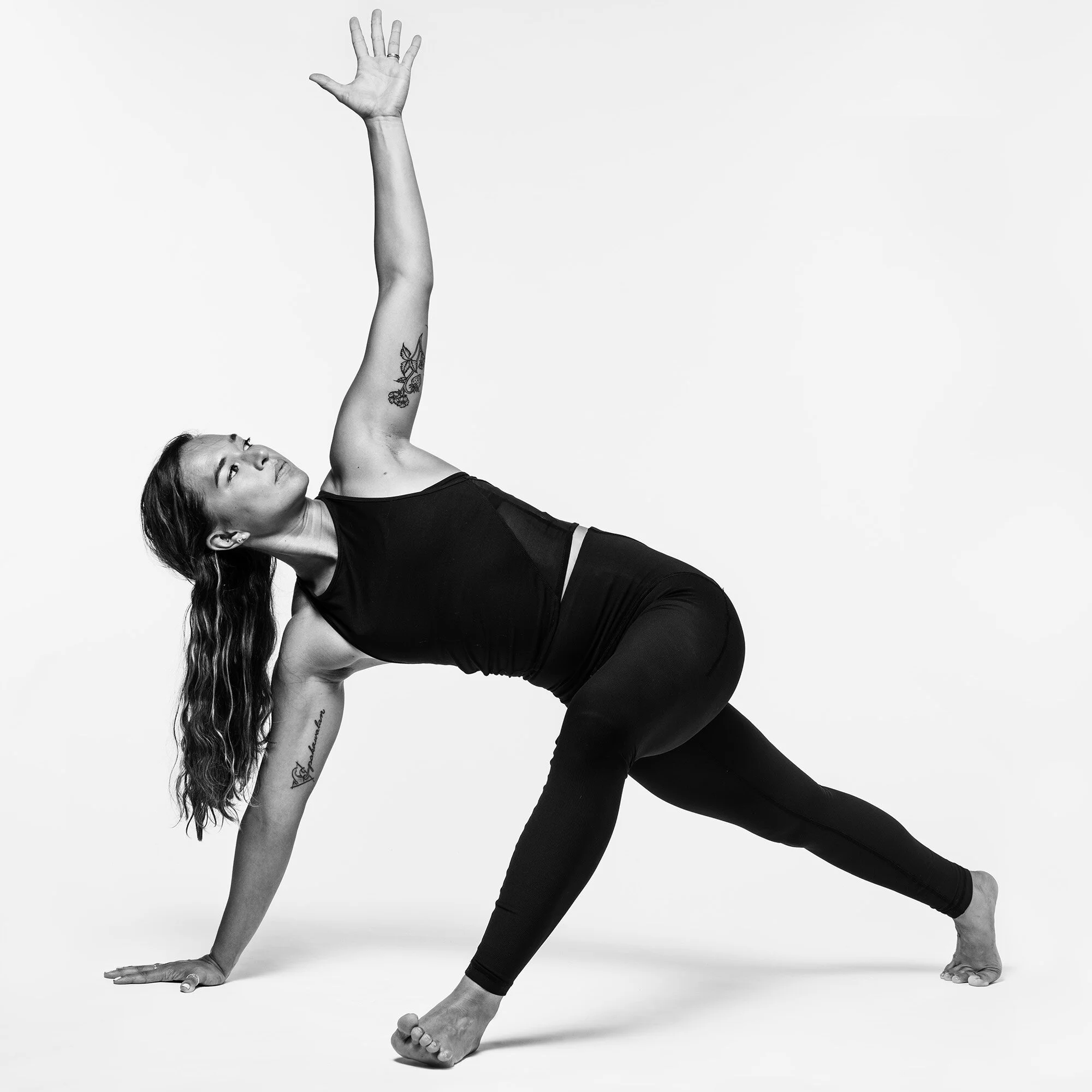A woman practicing yoga in a side plank pose, with one arm raised and looking upwards, against a plain background.