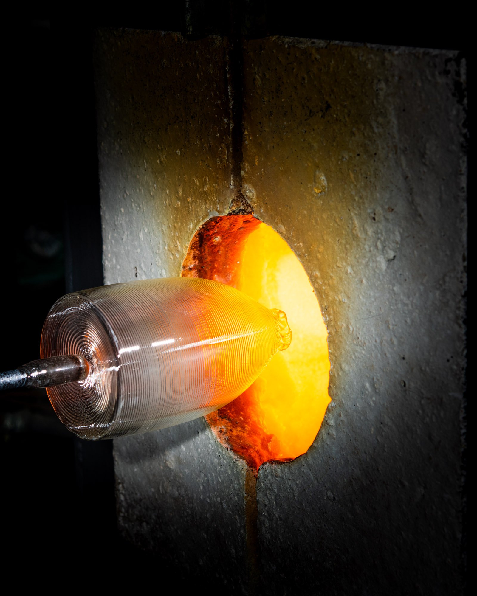 Glassblowing furnace with glowing orange and yellow molten glass being shaped.