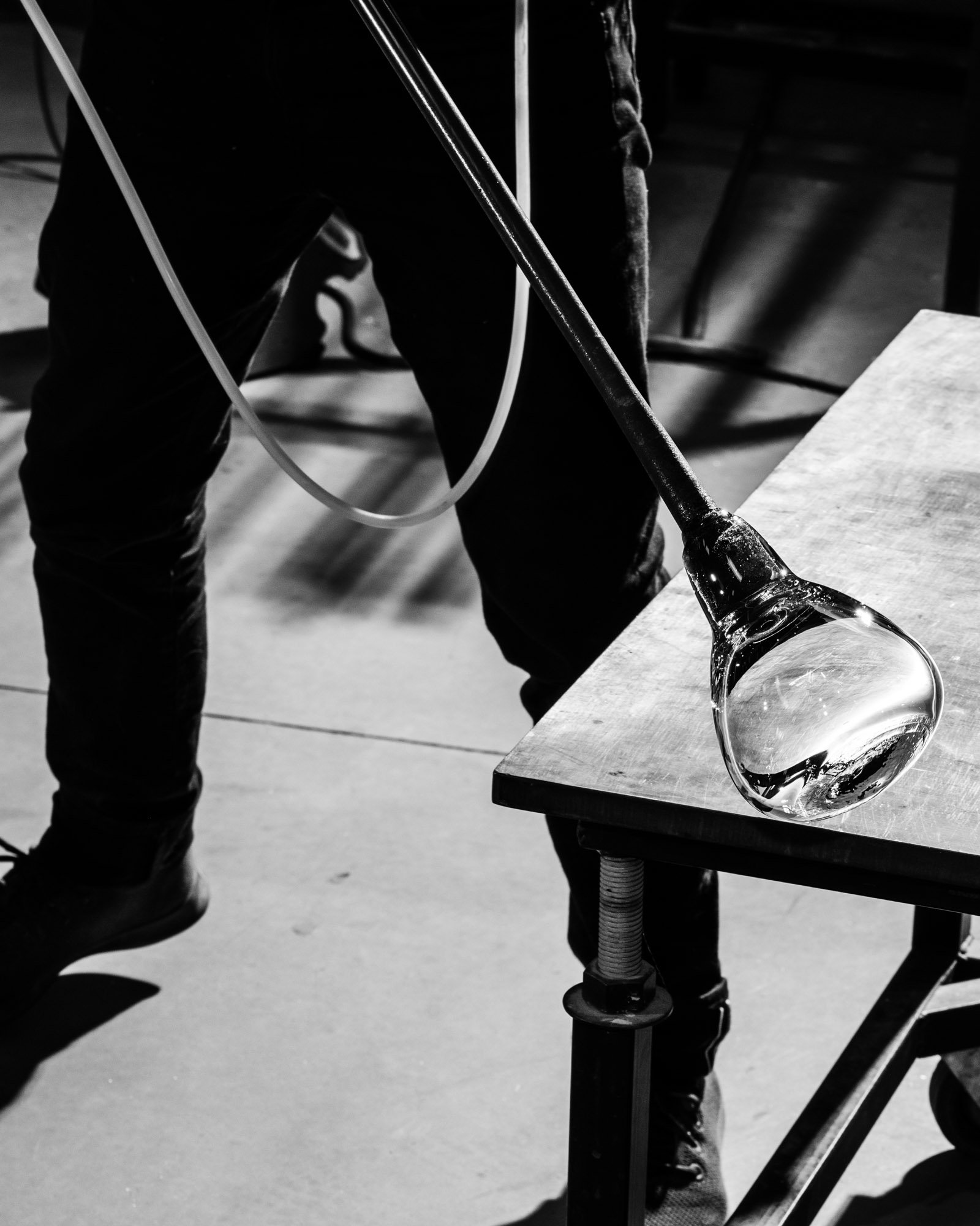 A person working with a glassblowing pipe in a studio, a large glass sphere is visible at the end of the pipe placed on a workbench.