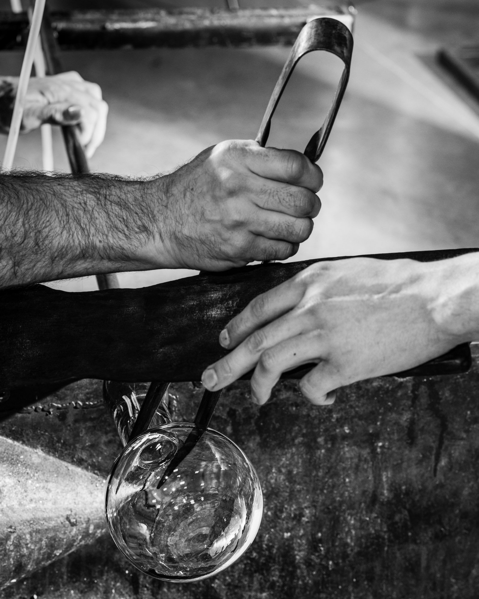 Close-up of a person's hairy arm holding a smartphone, with another person's hand holding a glass orb underneath, in black and white.