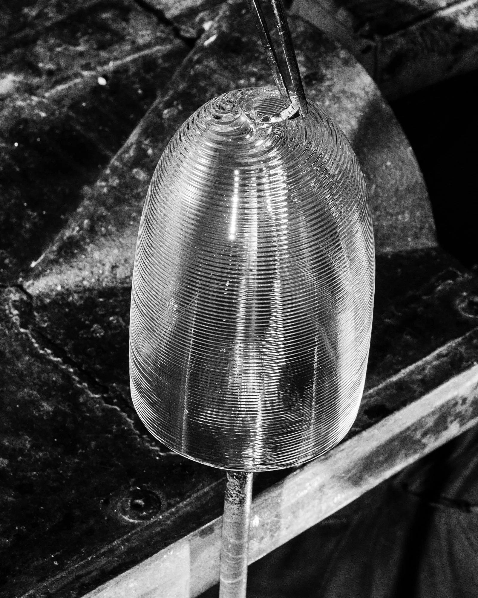 A glass vase being crafted on a lathe, with a tool shaping the glass.