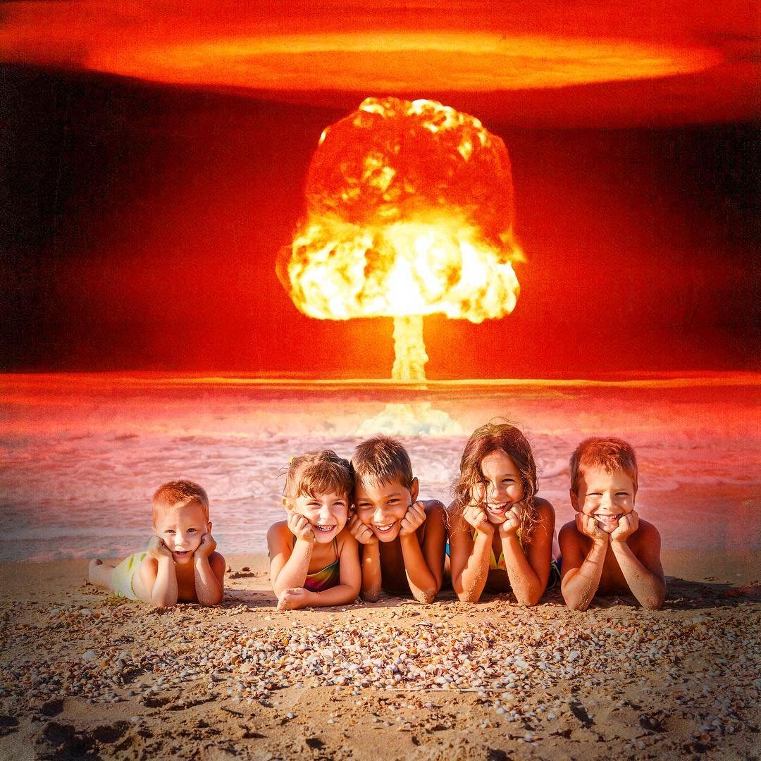 Five children lying on the beach with a nuclear explosion in the sky behind them.