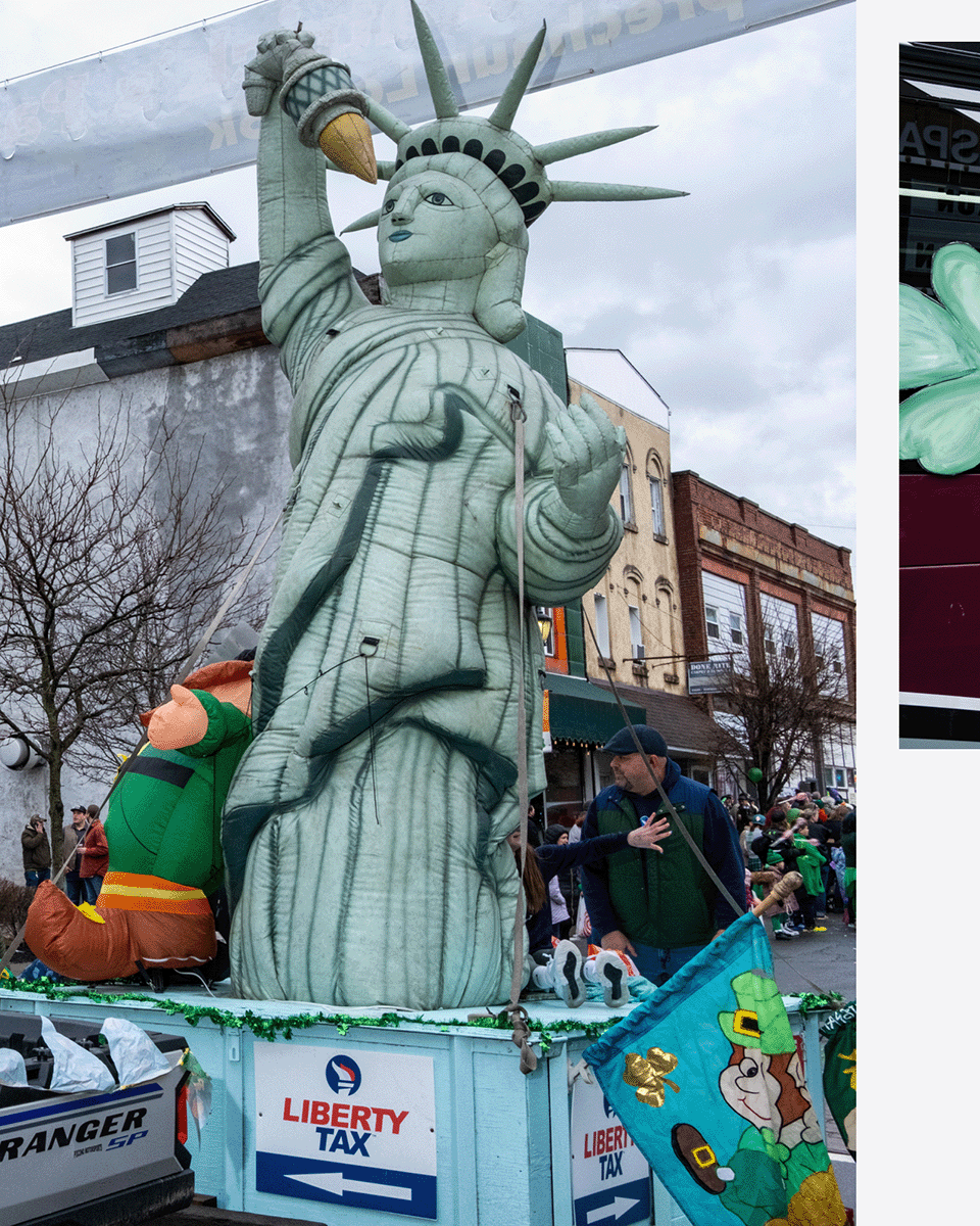 A parade float featuring a giant Statue of Liberty with a humorous twist, holding a giant turkey leg. The float displays a sign that reads 'Liberty Tax' and is decorated with green shamrocks and a leprechaun flag, indicating an Irish or St. Patrick's