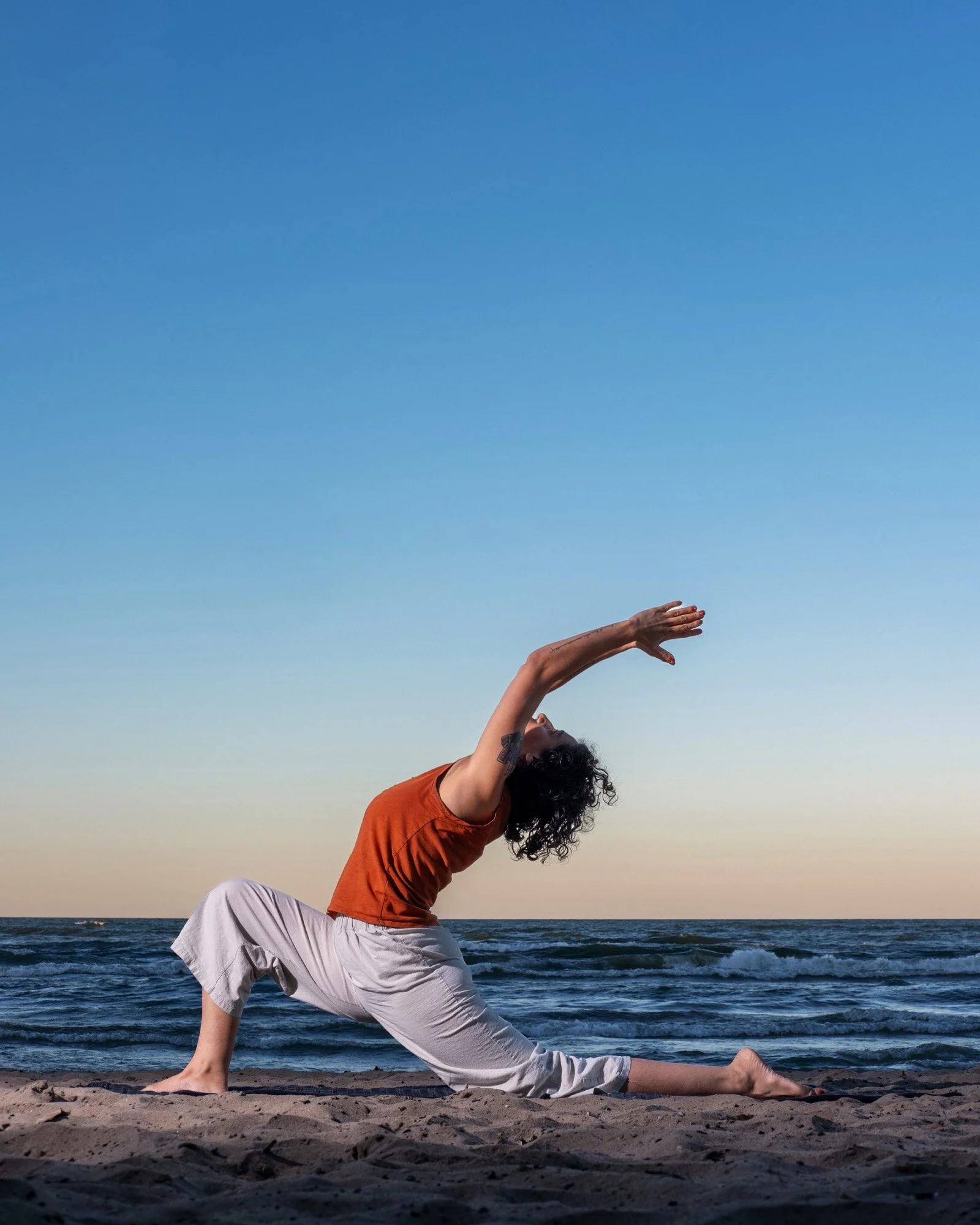A person practicing yoga on a beach during sunset, with blue sky and calm ocean in the background.