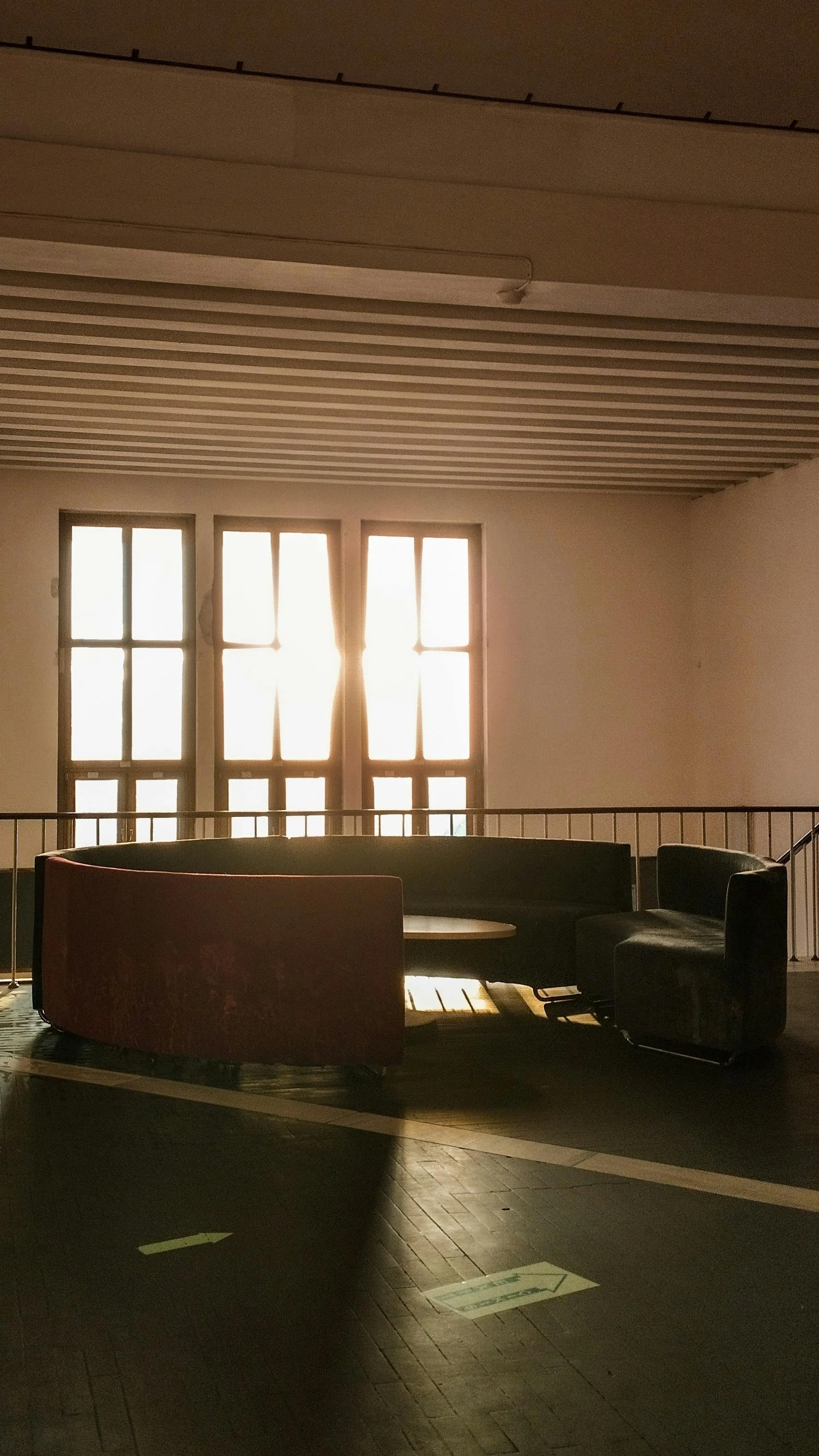 Ein heller Raum mit großen Fenstern, die Sonnenlicht durchlassen, und Sitzgelegenheiten darunter.