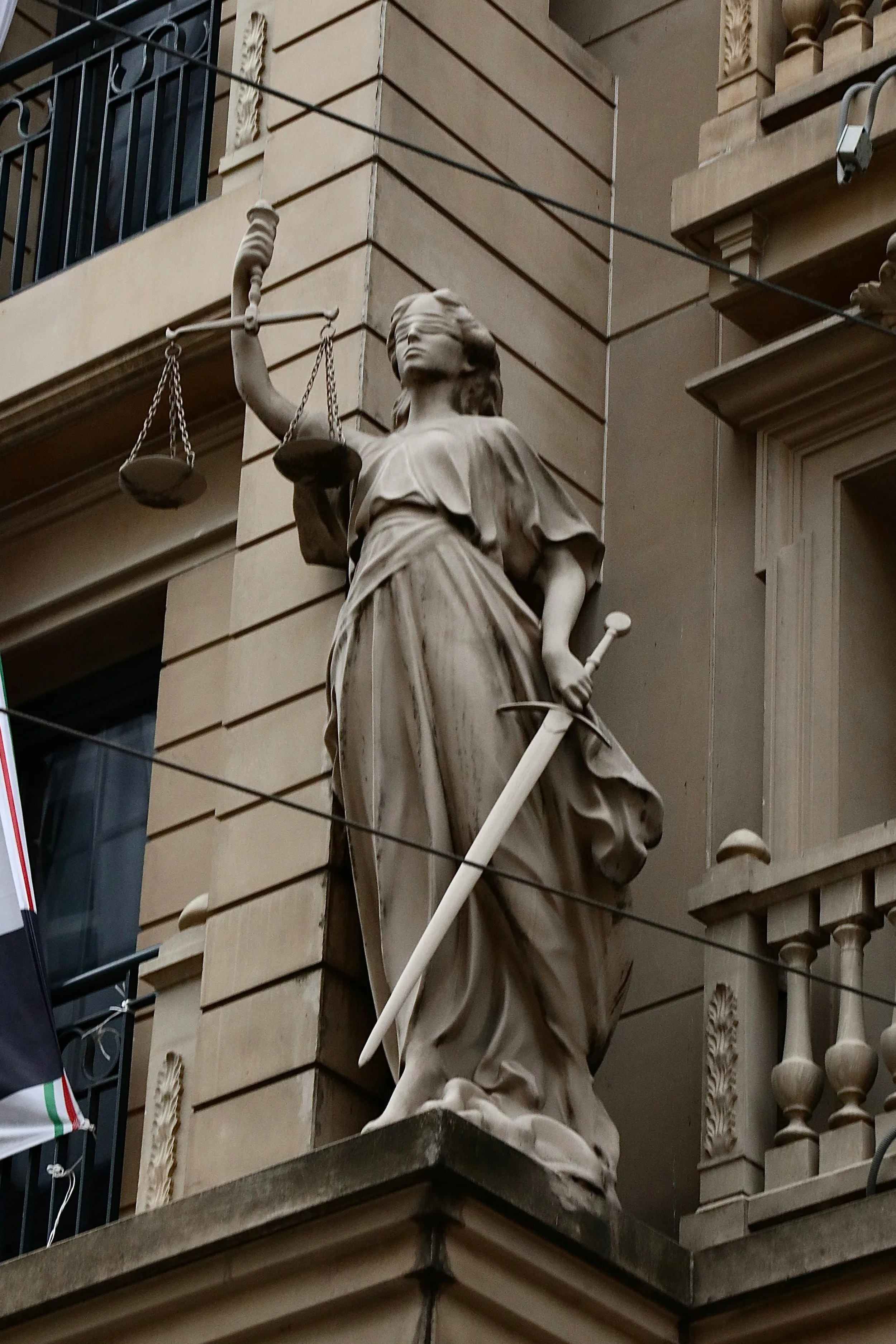 Statue der Justitia auf einem Balkon an einem historischen Gebäude.