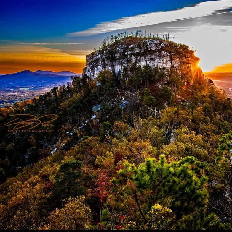 A mountain covered in trees during sunset, with a partly cloudy sky in the background.