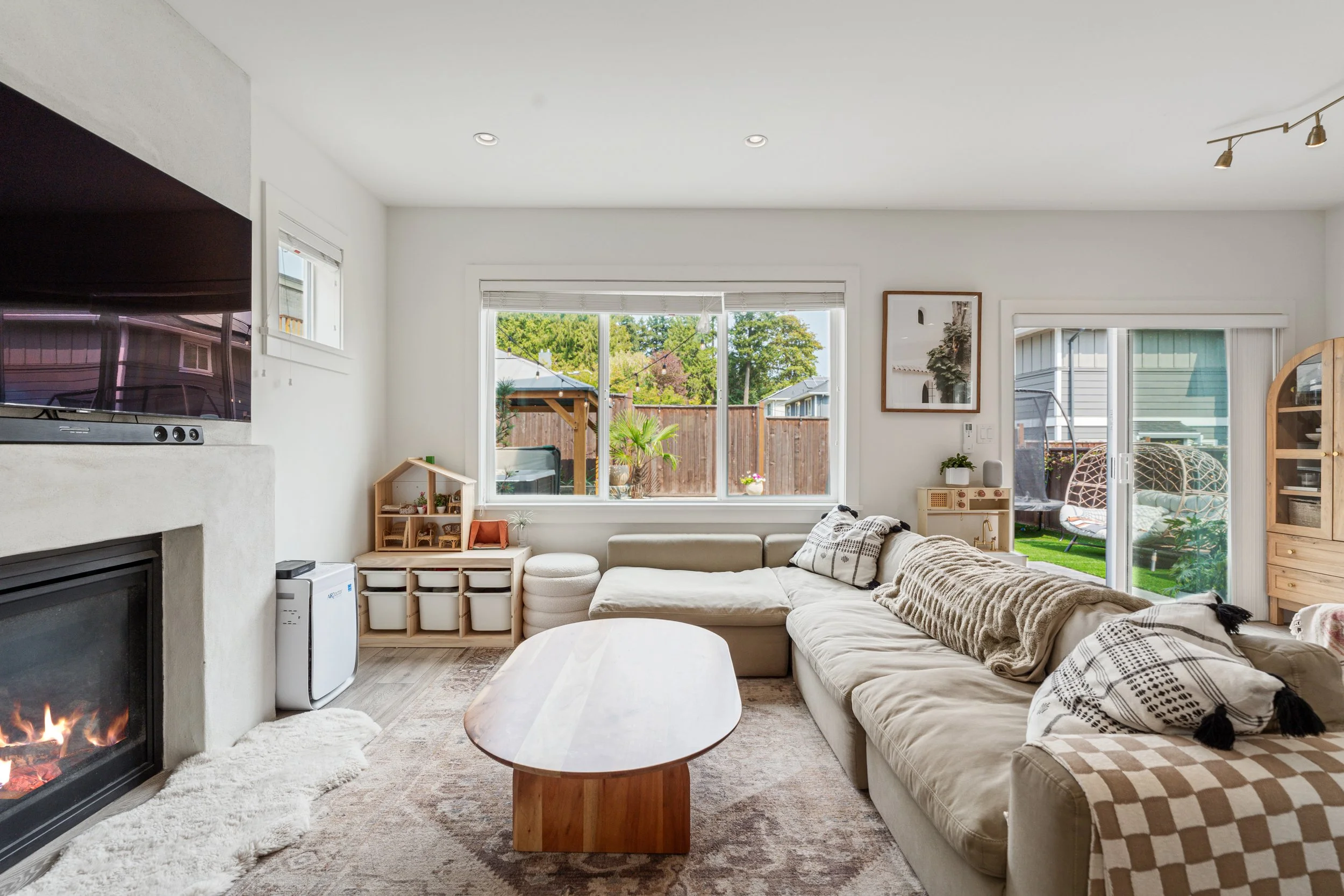 Bright, cozy living room with a fireplace, sectional sofa, large windows, and sliding glass doors opening to a landscaped backyard.