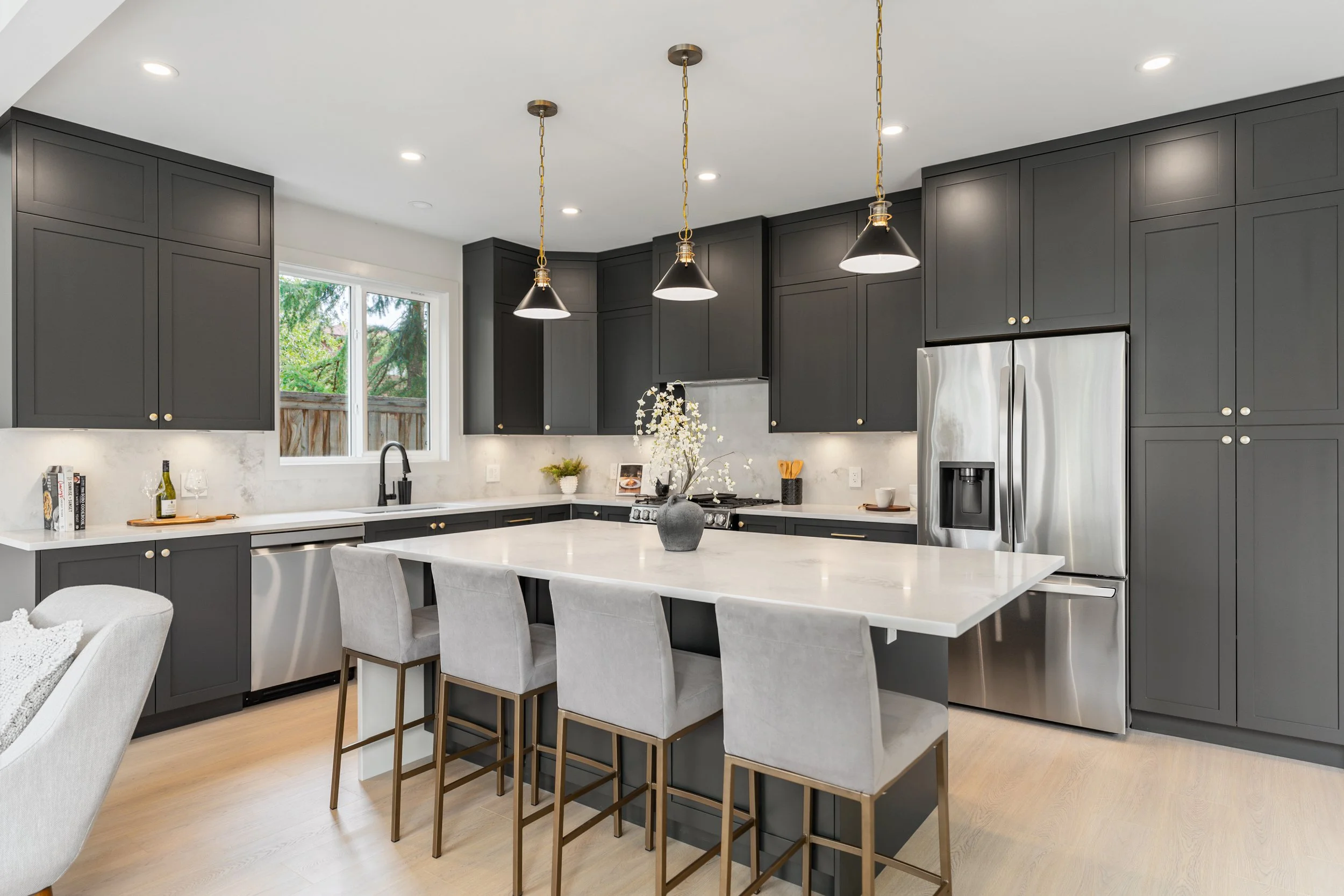 Modern kitchen with dark gray cabinetry, white countertops, stainless steel appliances, and a large island with seating.