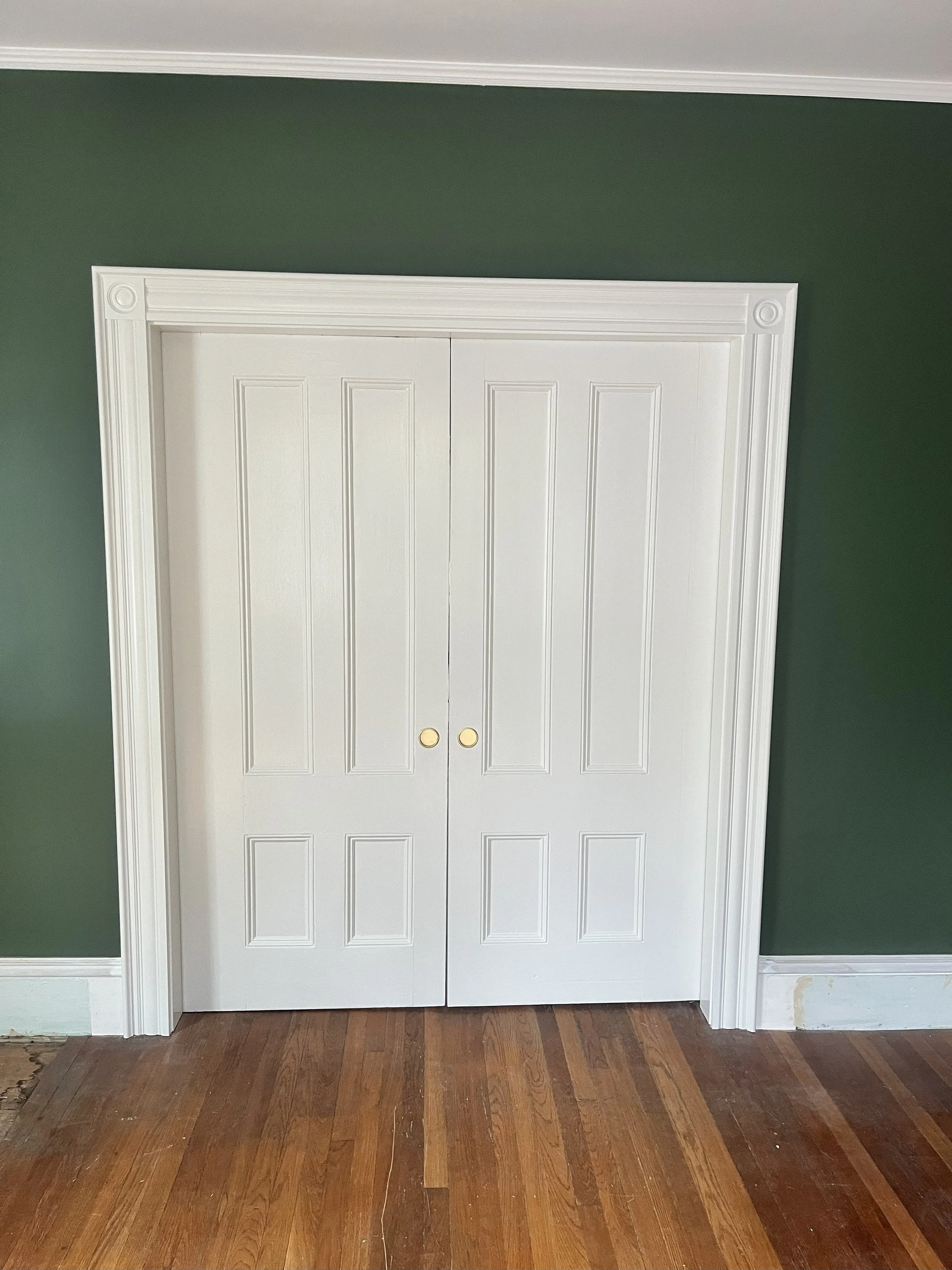 White double closet doors with decorative molding in a room with dark green walls and hardwood floors.
