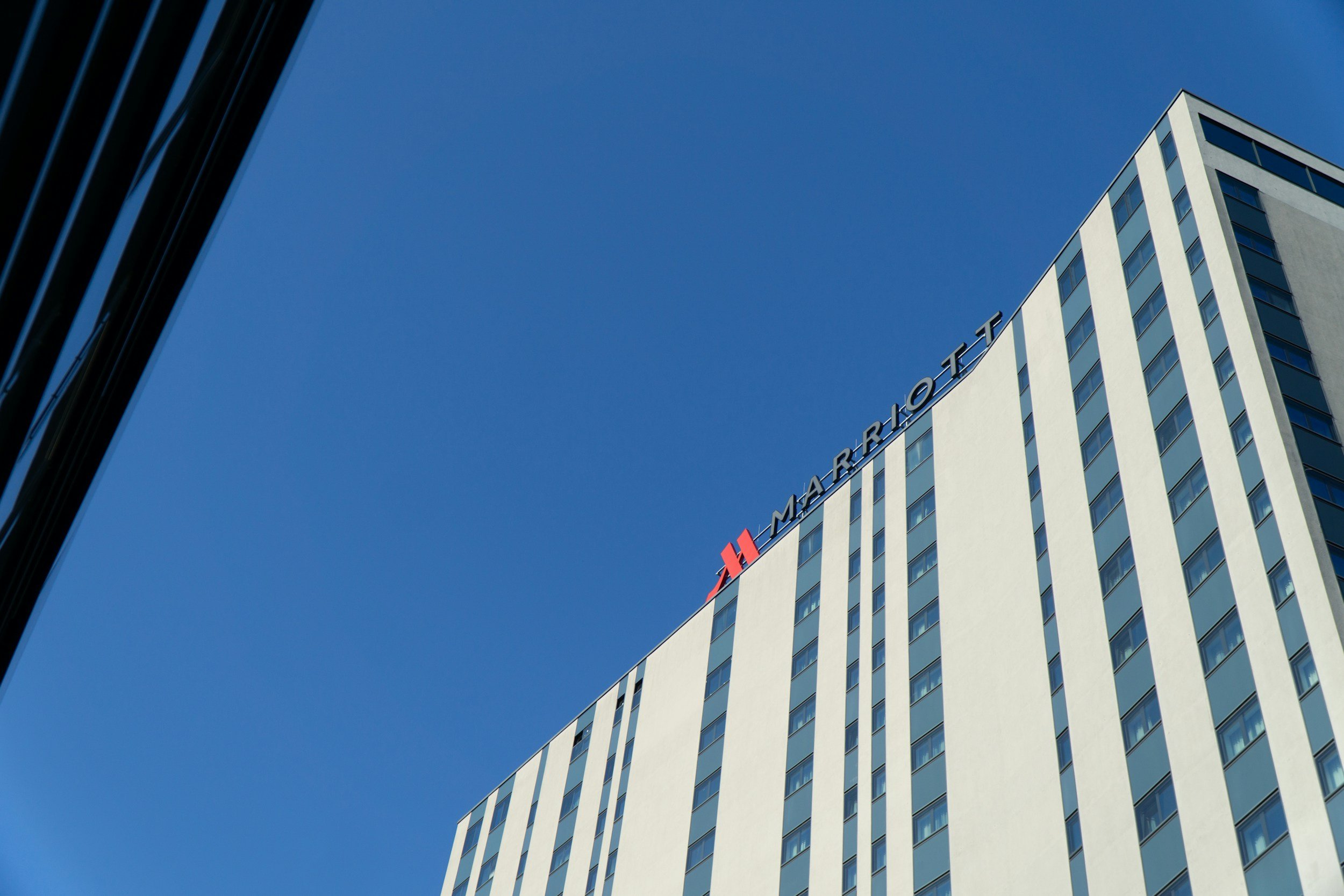 Low-angle view of a tall, modern hotel building with the name 'Marriott' displayed at the top, under a clear blue sky.
