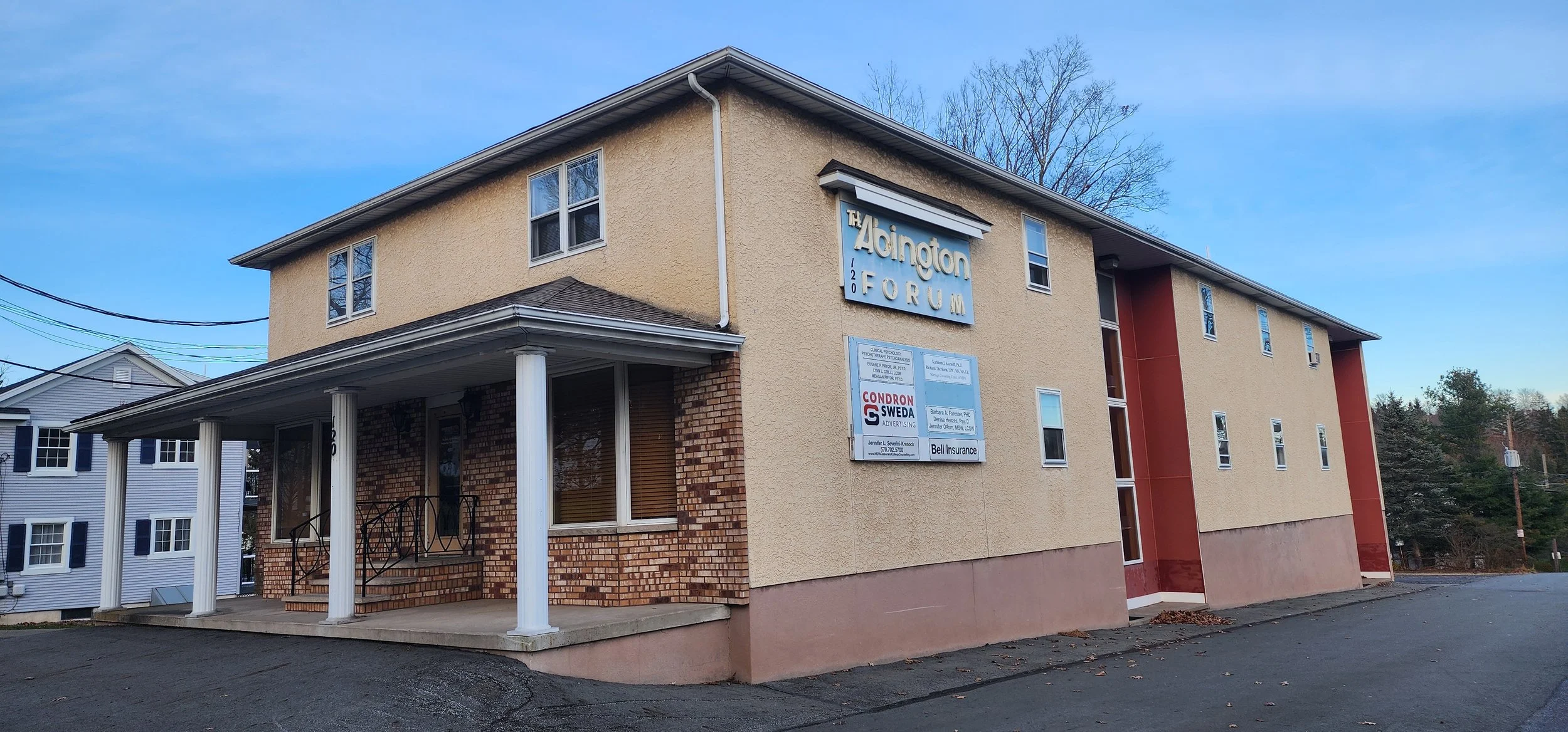 A two-story beige building with a red accent wall and white columns at the entrance, featuring a sign that reads 'The Adington Forum 120' and additional smaller signs on the front.