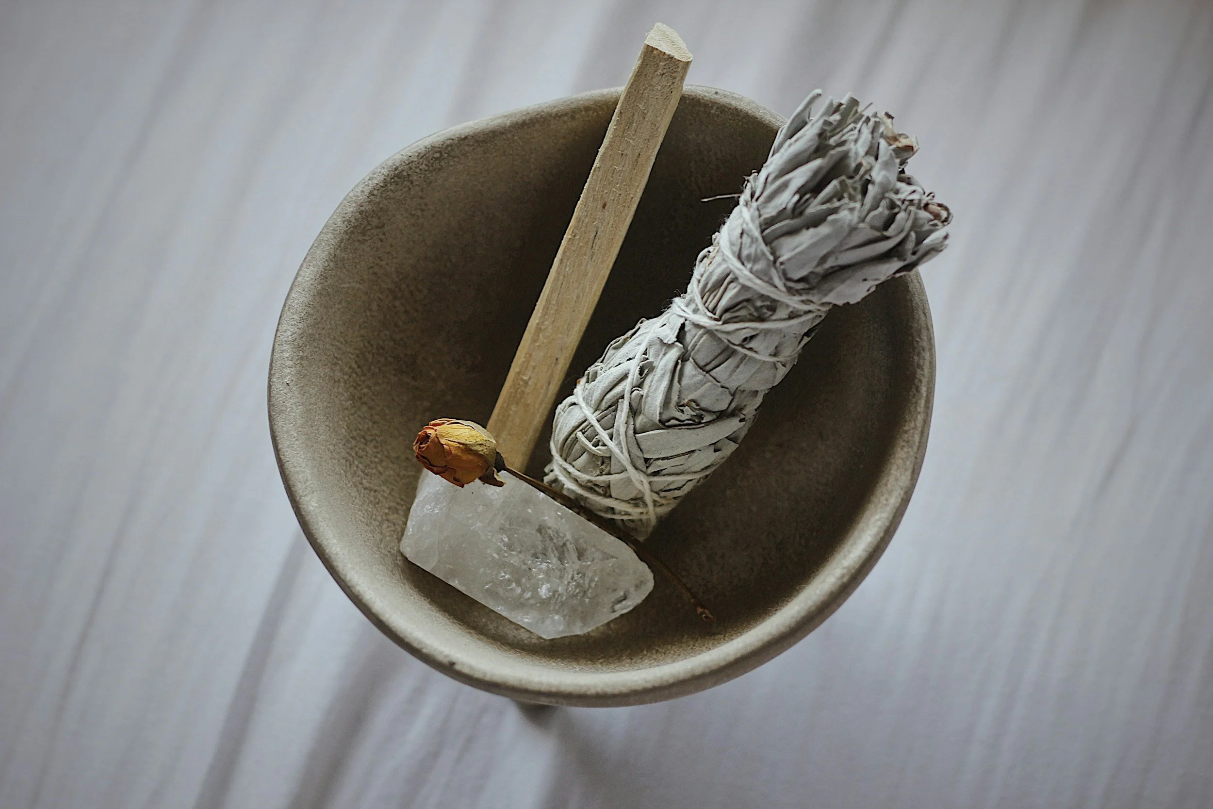 A mortar and pestle with sage smudging bundle, a palo santo stick, and a crystal in the mortar.