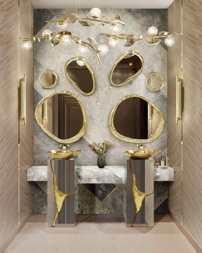 Modern bathroom with marble sinks and gold-accented mirrors, decorative lighting, and a vase with flowers.