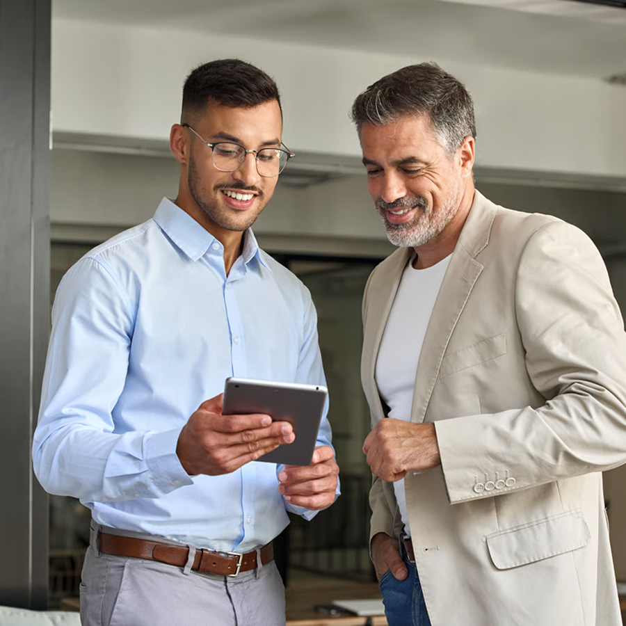 Two men looking at a tablet together in an indoor setting, smiling and engaged in conversation.