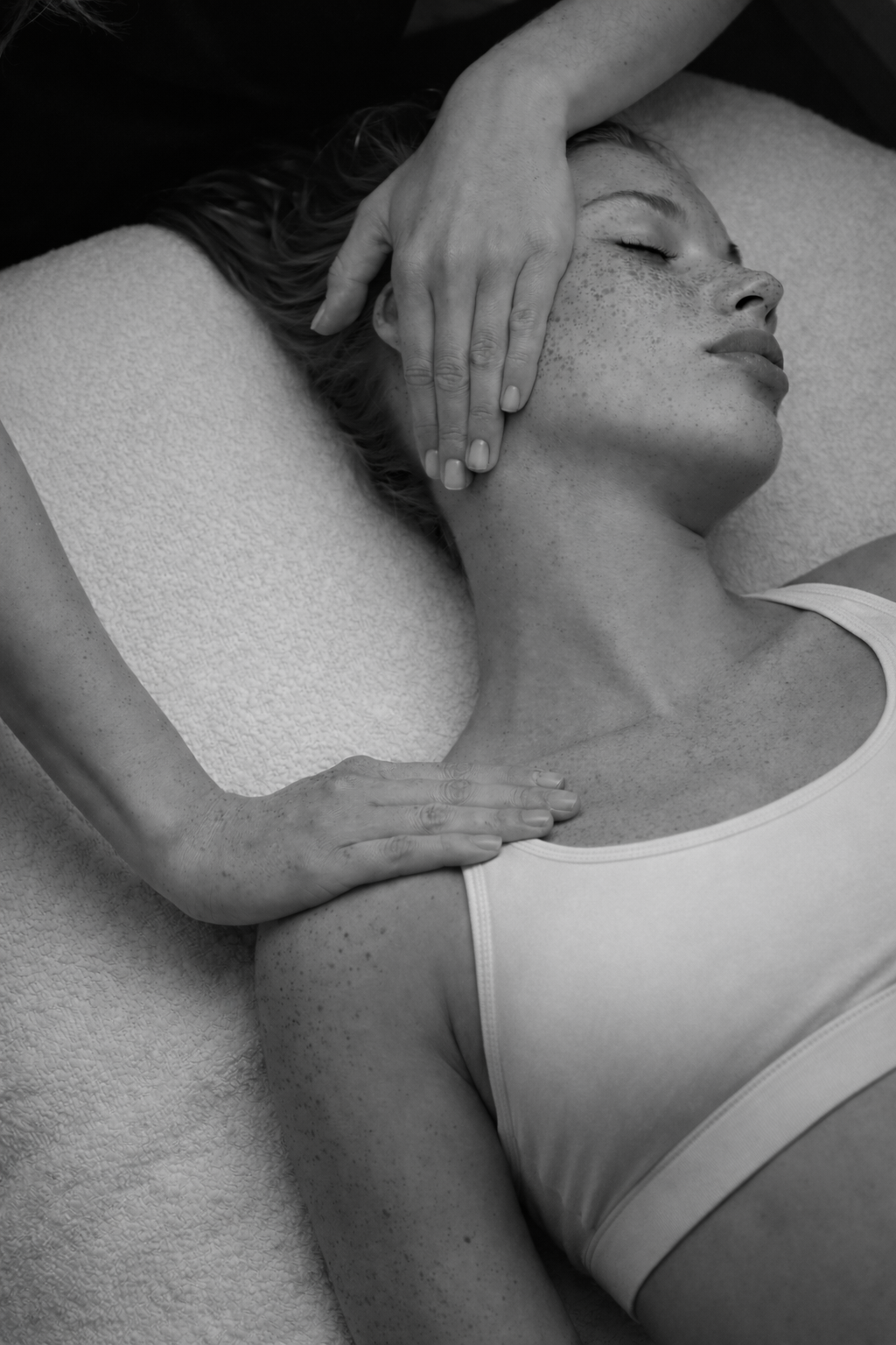 Femme allongée avec un visage détendu, yeux fermés, recevant une séance de massage du visage, sur une surface douce.