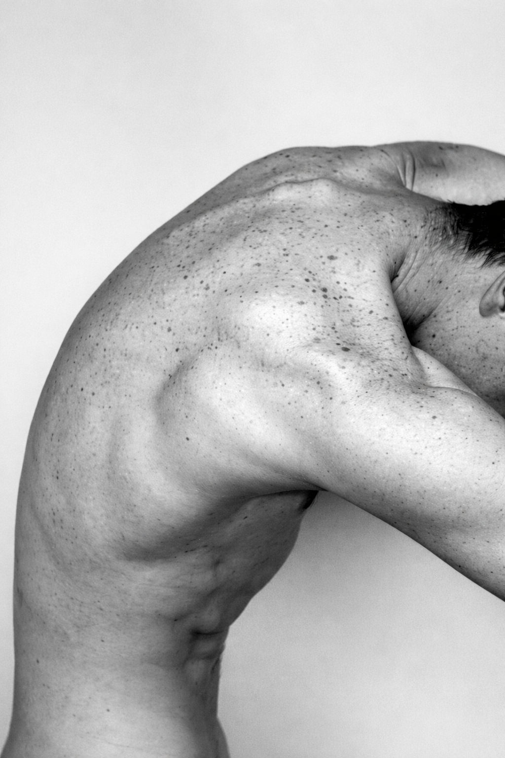 Un homme nu, vu de côté, avec un torse musclé et la tête inclinée, sur un fond blanc.