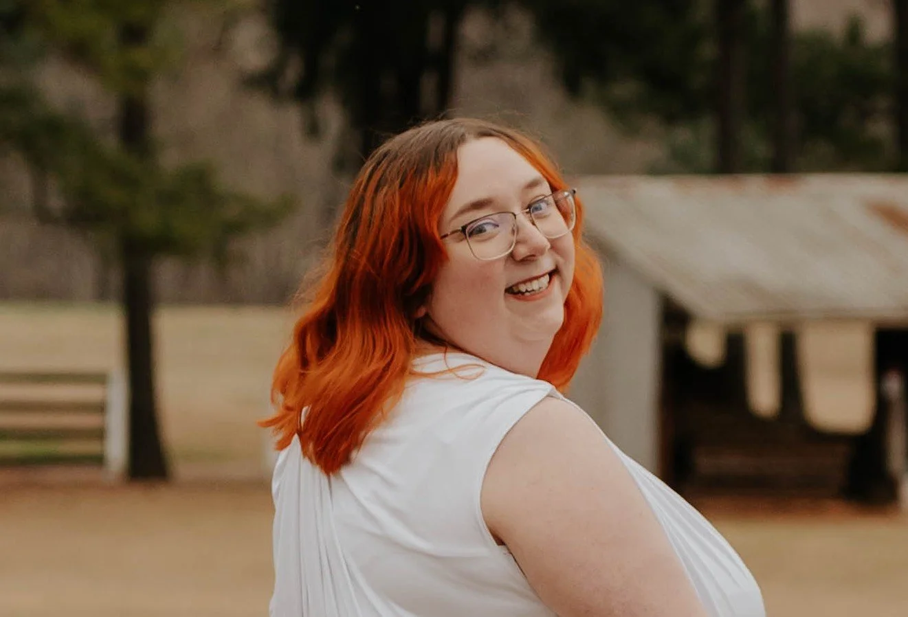 Girl with red hair and glasses smiling with a white dress.