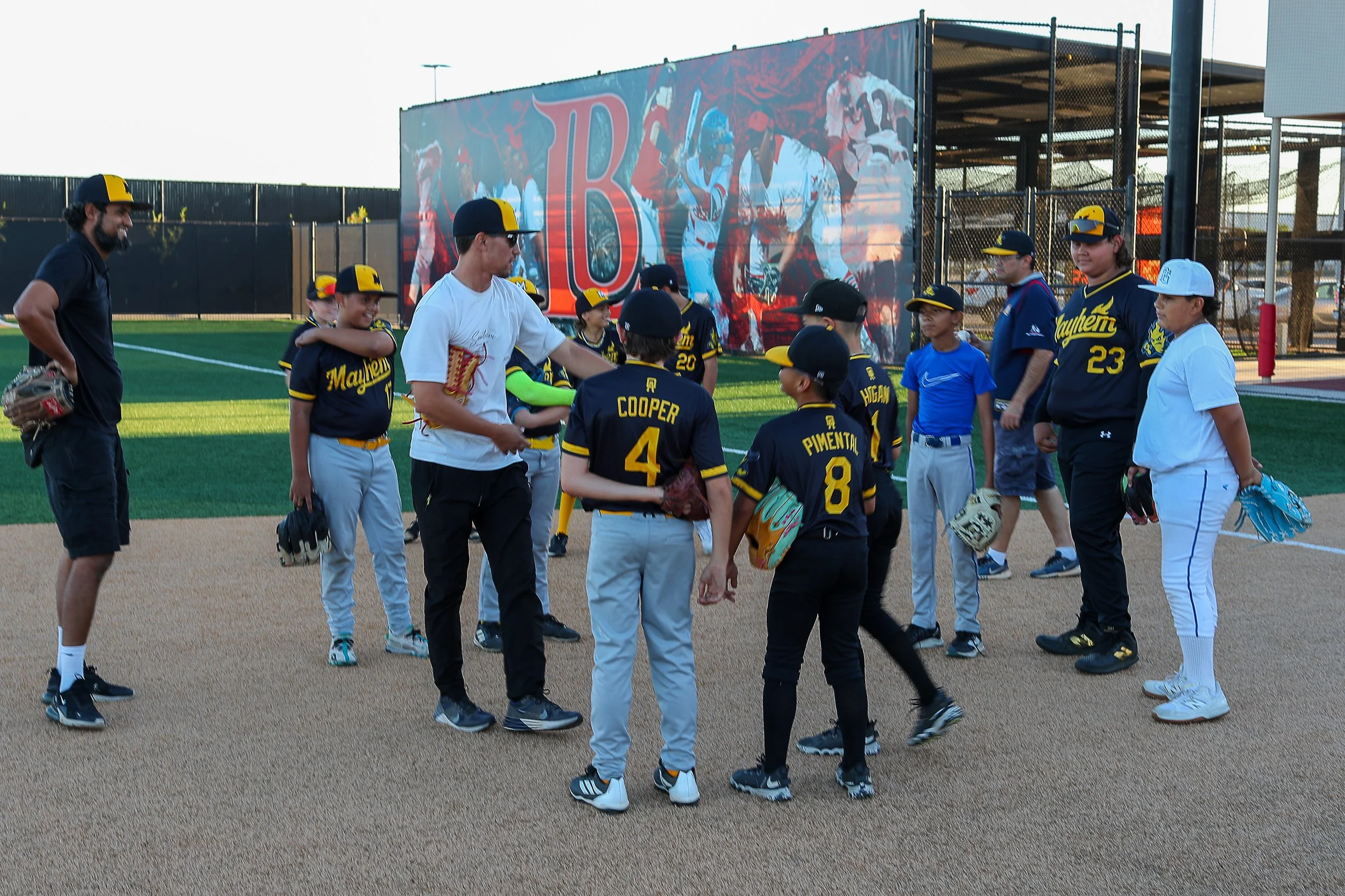 Youth baseball team receiving instructions on the field while coaches and parents watch.