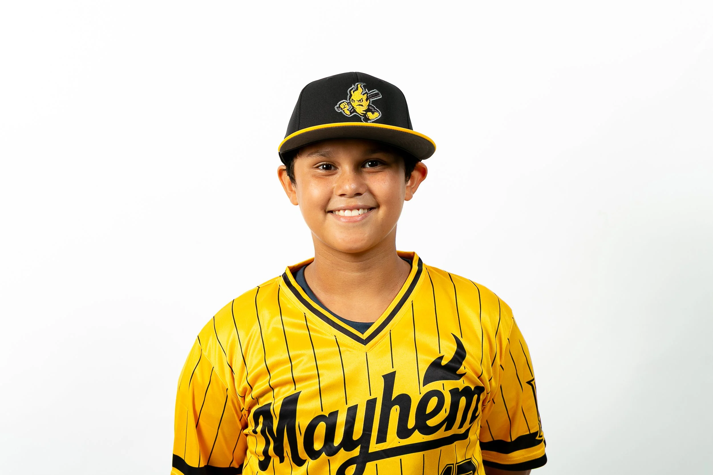 A young boy smiling, wearing a black baseball cap with a yellow brim and a logo, and a yellow sports jersey with black pinstripes and the word 'Mayhem' on it.