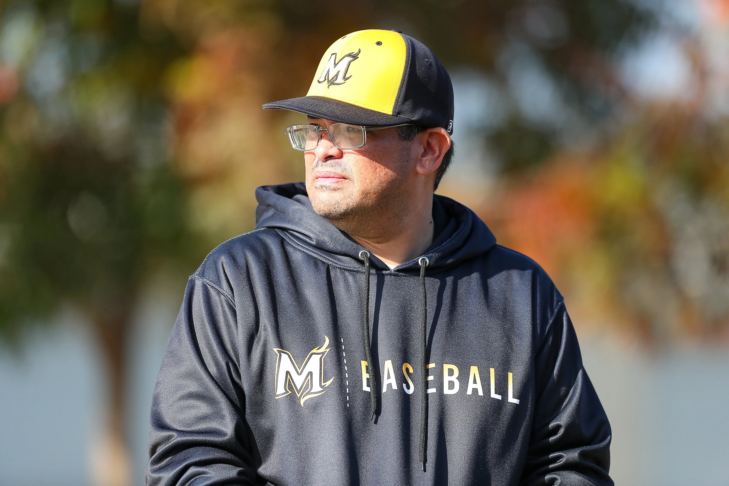 Coach Richard looking out into the distance wearing a black hat with an M logo on it.