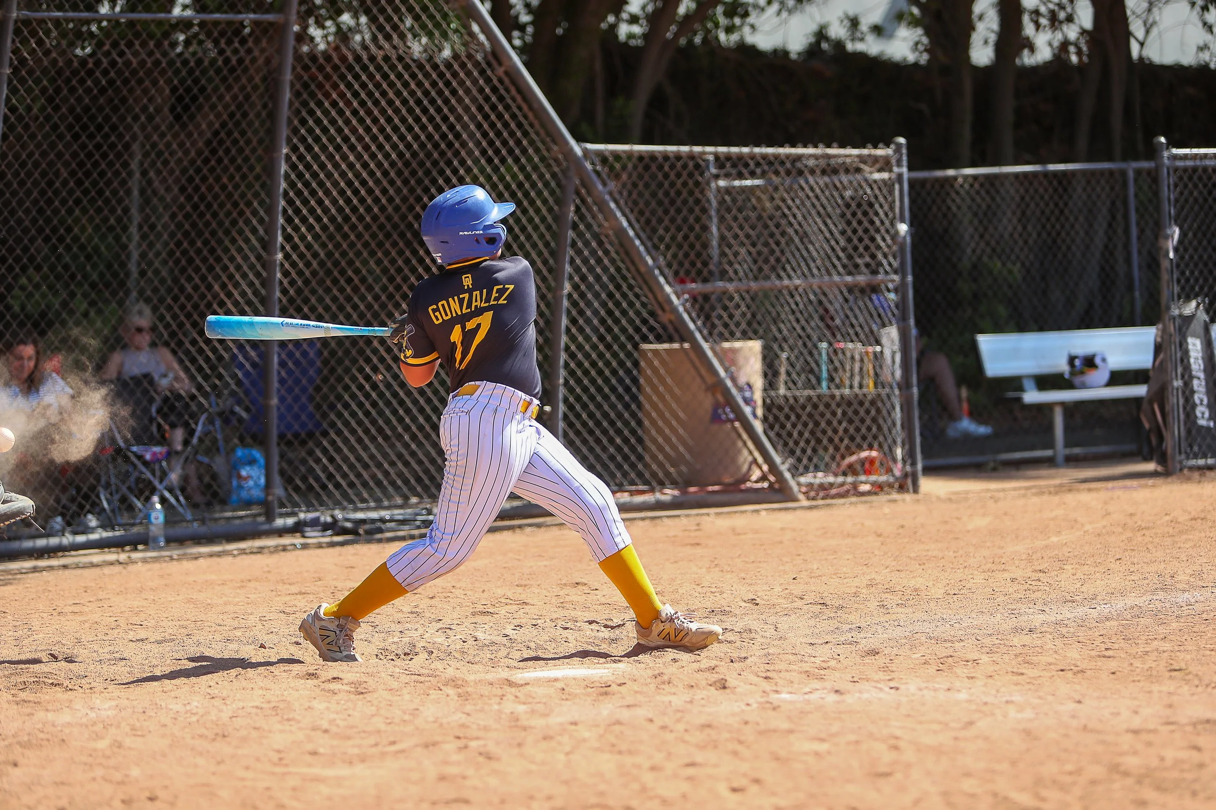 A young baseball player in a blue helmet and striped pants swings a bat on a dirt field during a game.
