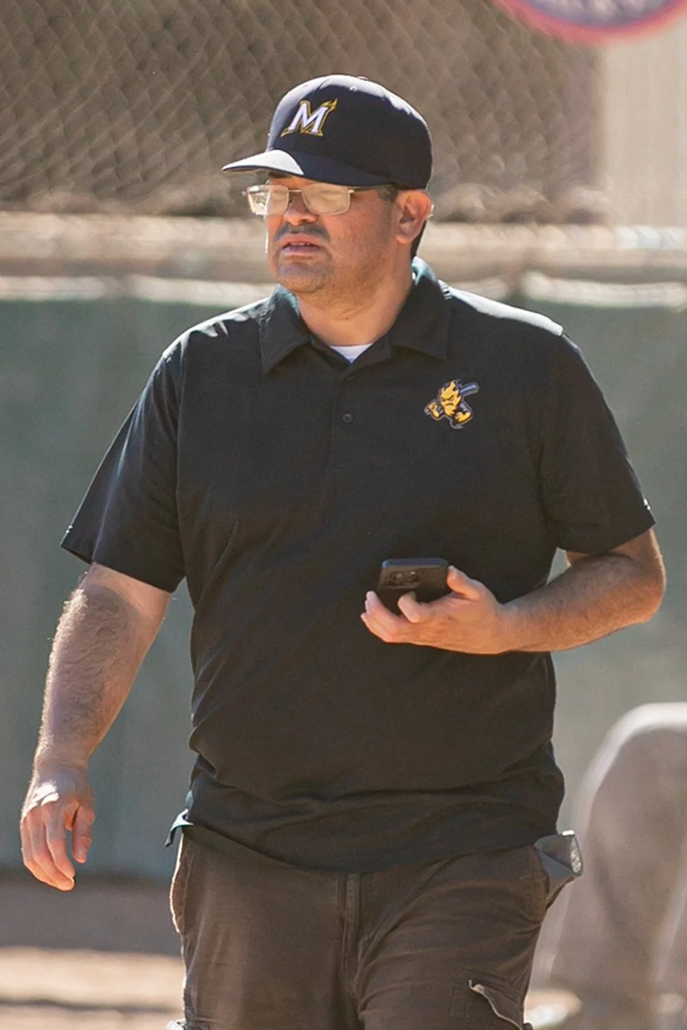 Coach Richard looking out into the distance wearing a black hat with an M logo on it.