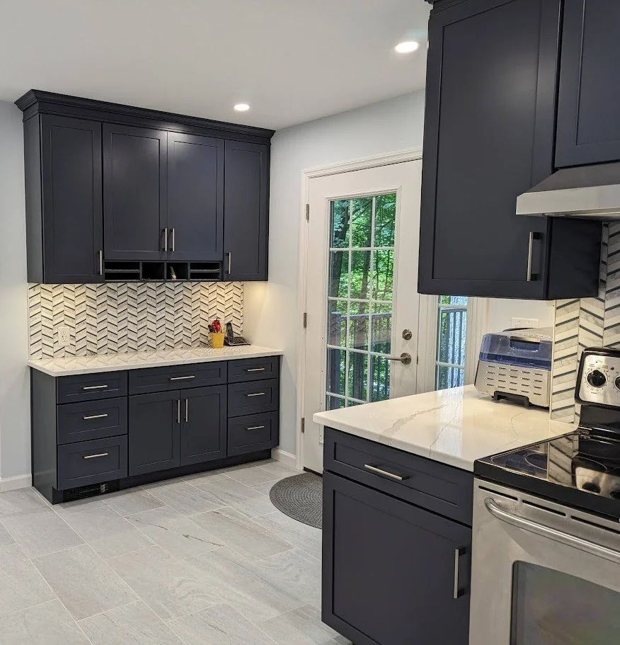 Modern kitchen with dark blue cabinets, white backsplash, white marble countertops, stainless steel appliances, and a glass door leading outside.