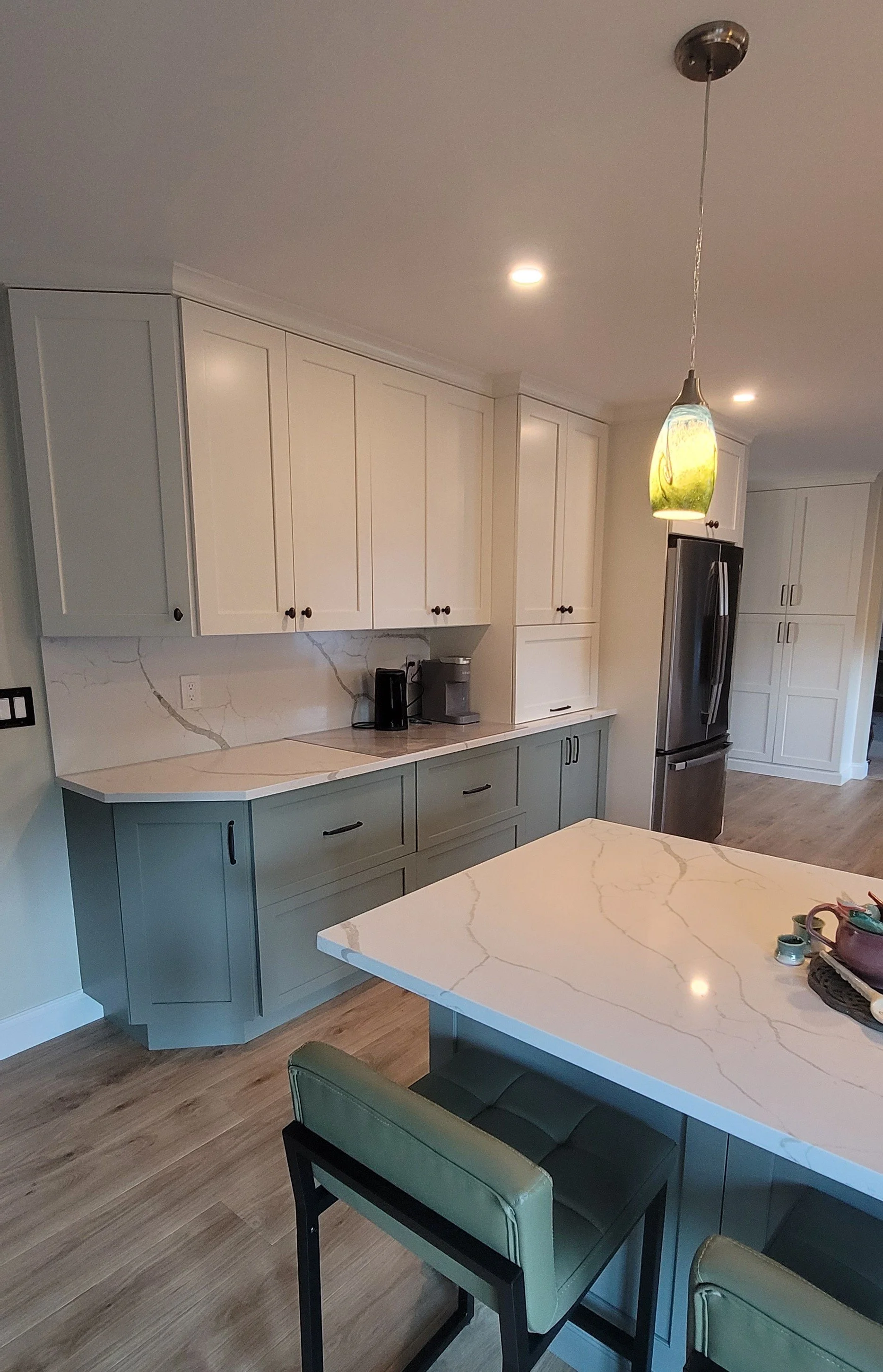 Cozy kitchen with dark green cabinets, white marble countertops, a white farmhouse sink, and open shelves with decorative items. Natural light from a window brightens the space, which is decorated with flowers, plants, and vintage accents.