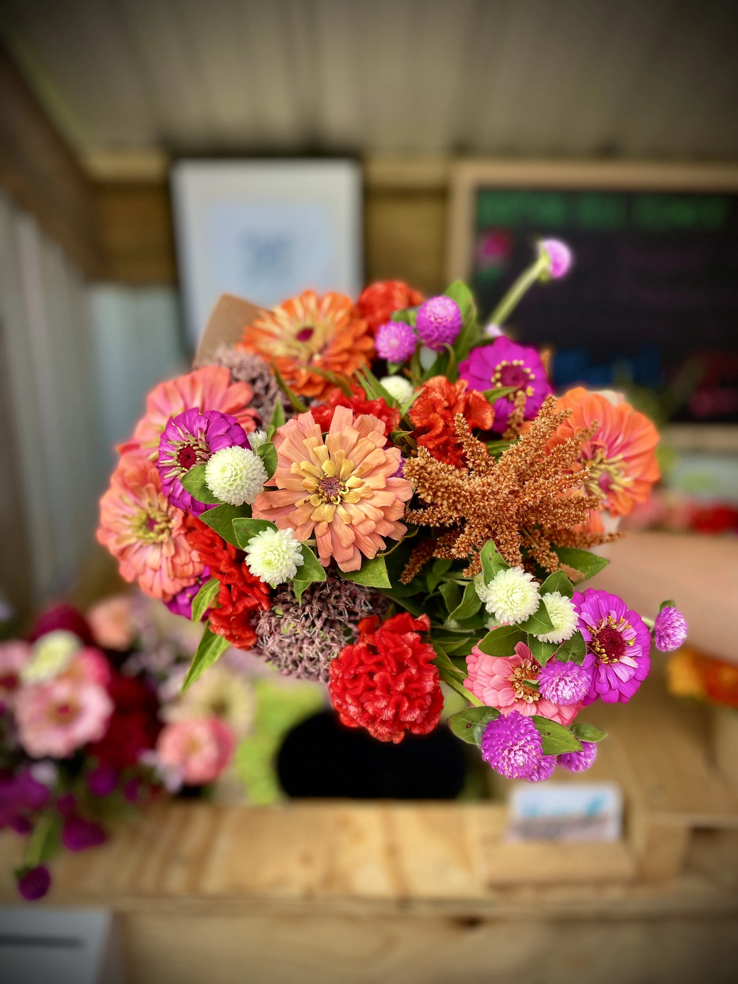 Colorful bouquet of flowers with pink, orange, red, purple, and white blooms on a wooden table.