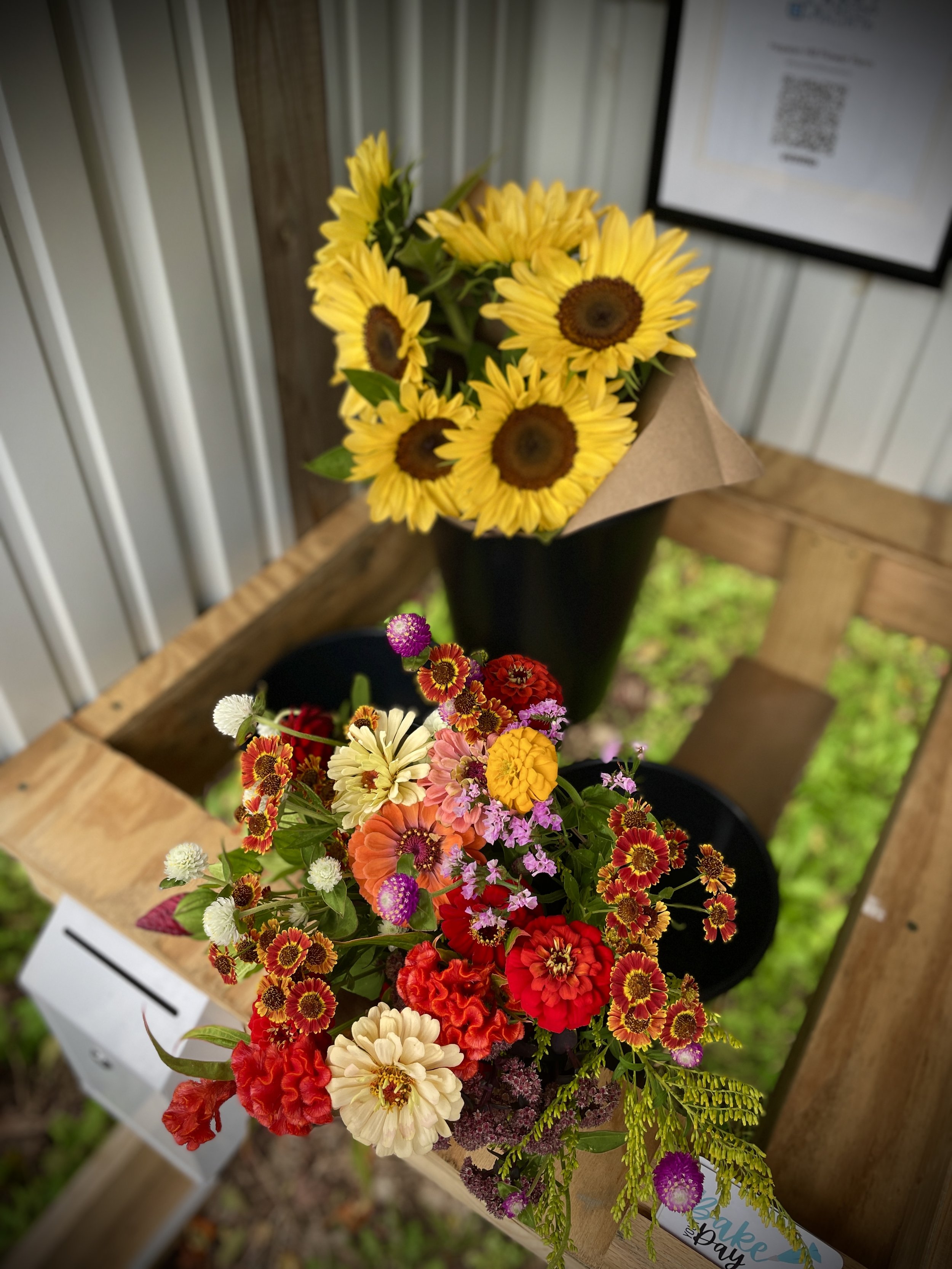 Colorful bouquet of flowers with sunflowers in a black vase and mixed smaller flowers on a wooden table.