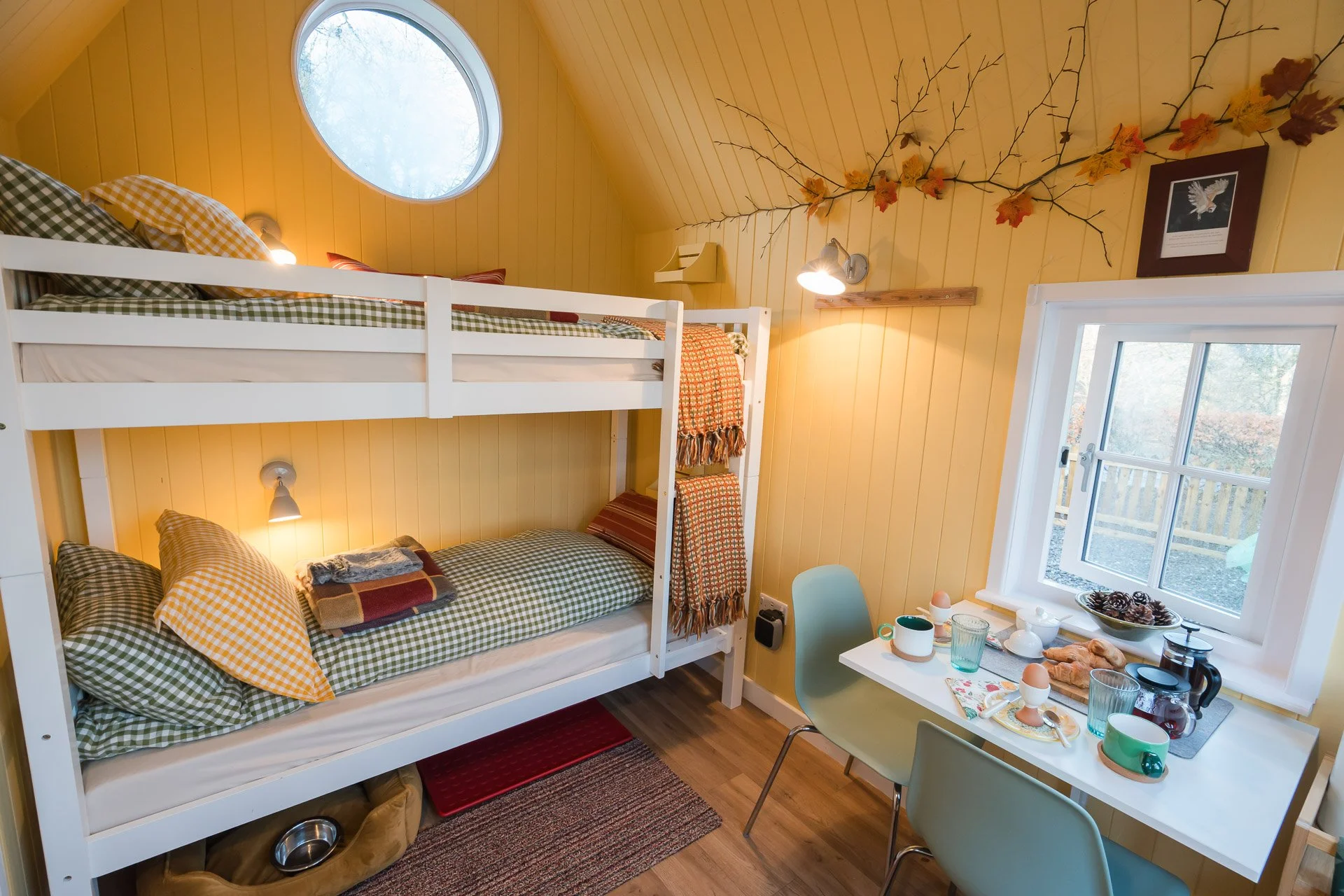 Cozy cabin bedroom with yellow paneled walls and a bunk bed, a window, and a small dining table set for breakfast.