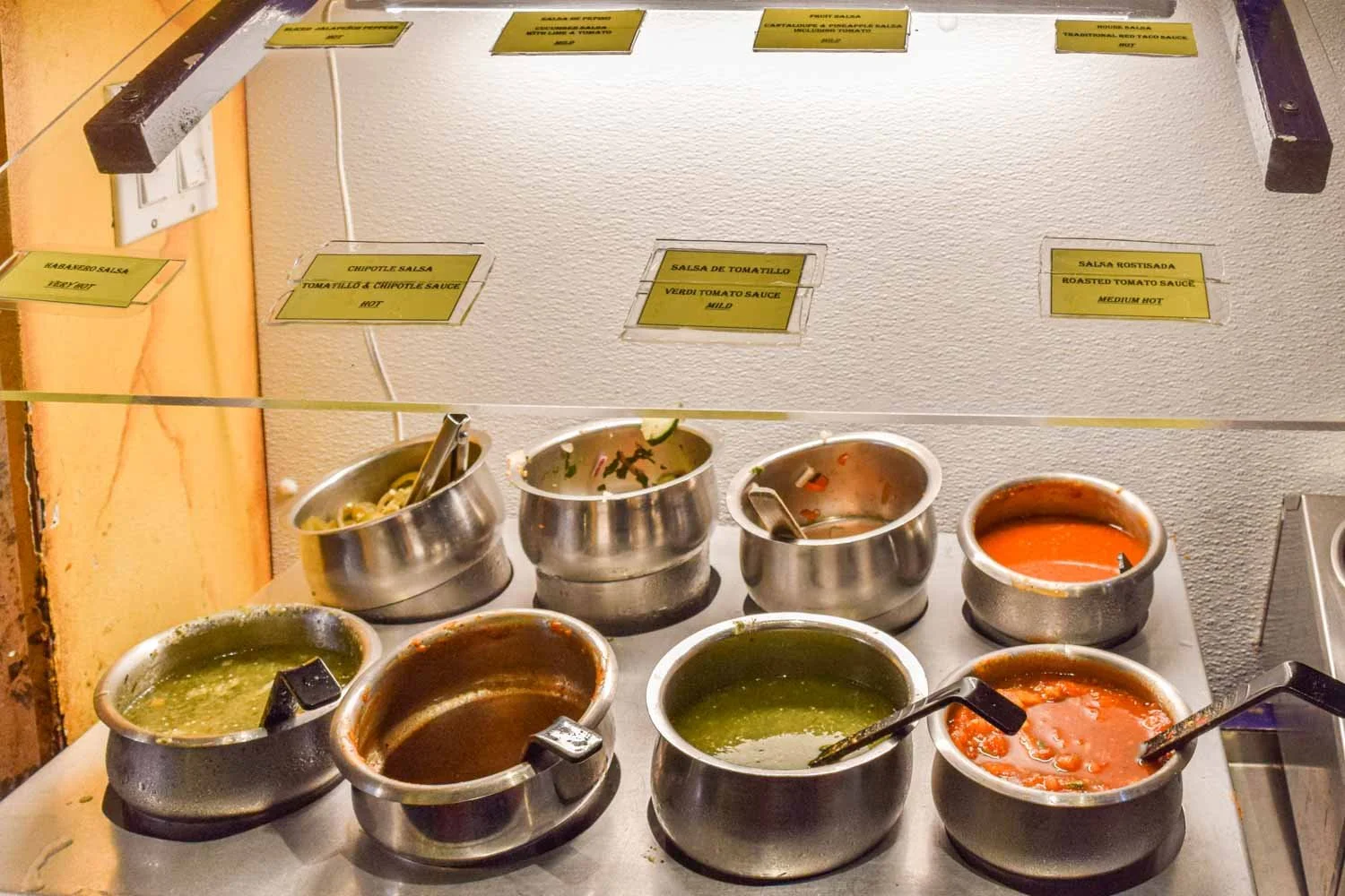 Variety of homemade red and green salsas in stainless steel containers at the El Metate salsa bar.