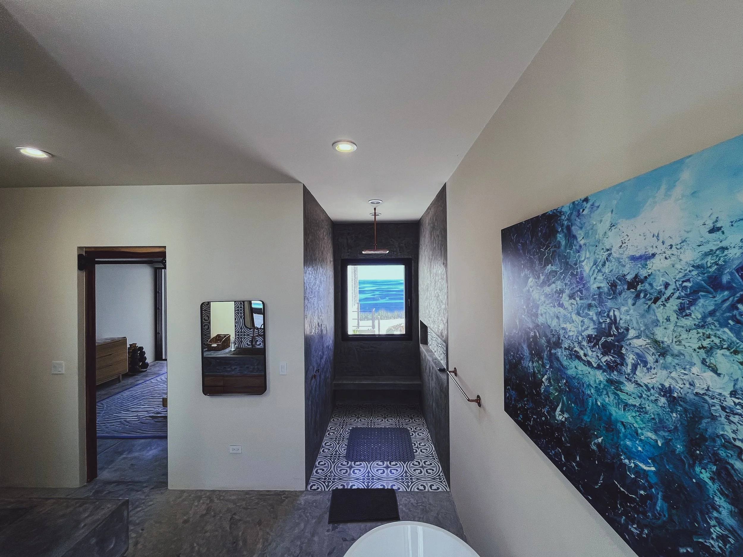 Interior space with a hallway leading to a window with a view, a colorful blue abstract painting on the wall, and a room visible on the left side.