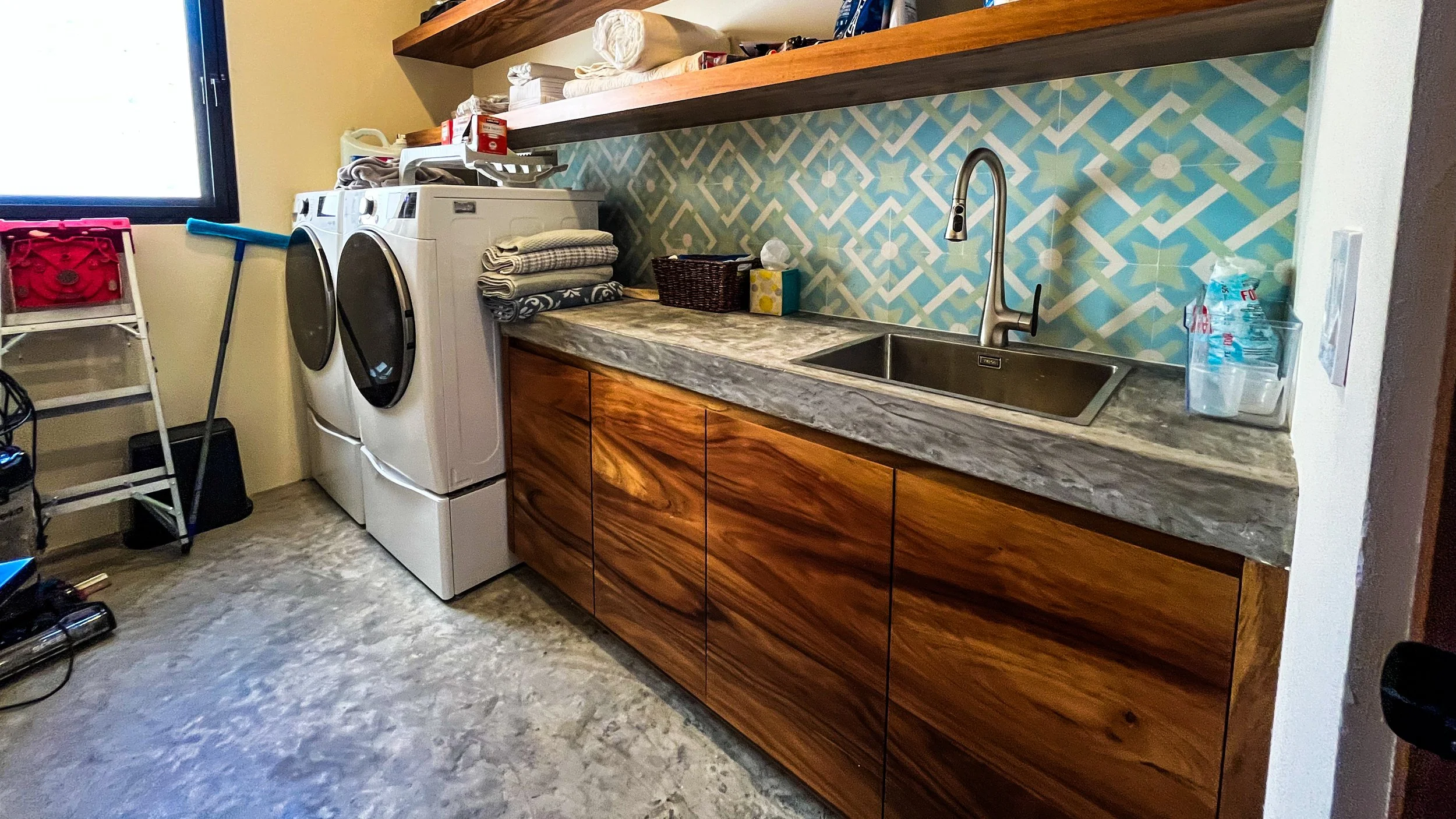 Laundry room with washing machine and dryer, wooden cabinets, marble countertop, and a backsplash with geometric pattern in blue, green, and white.