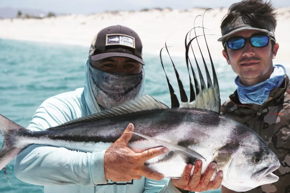 Two men holding a large fish on a boat in the ocean
